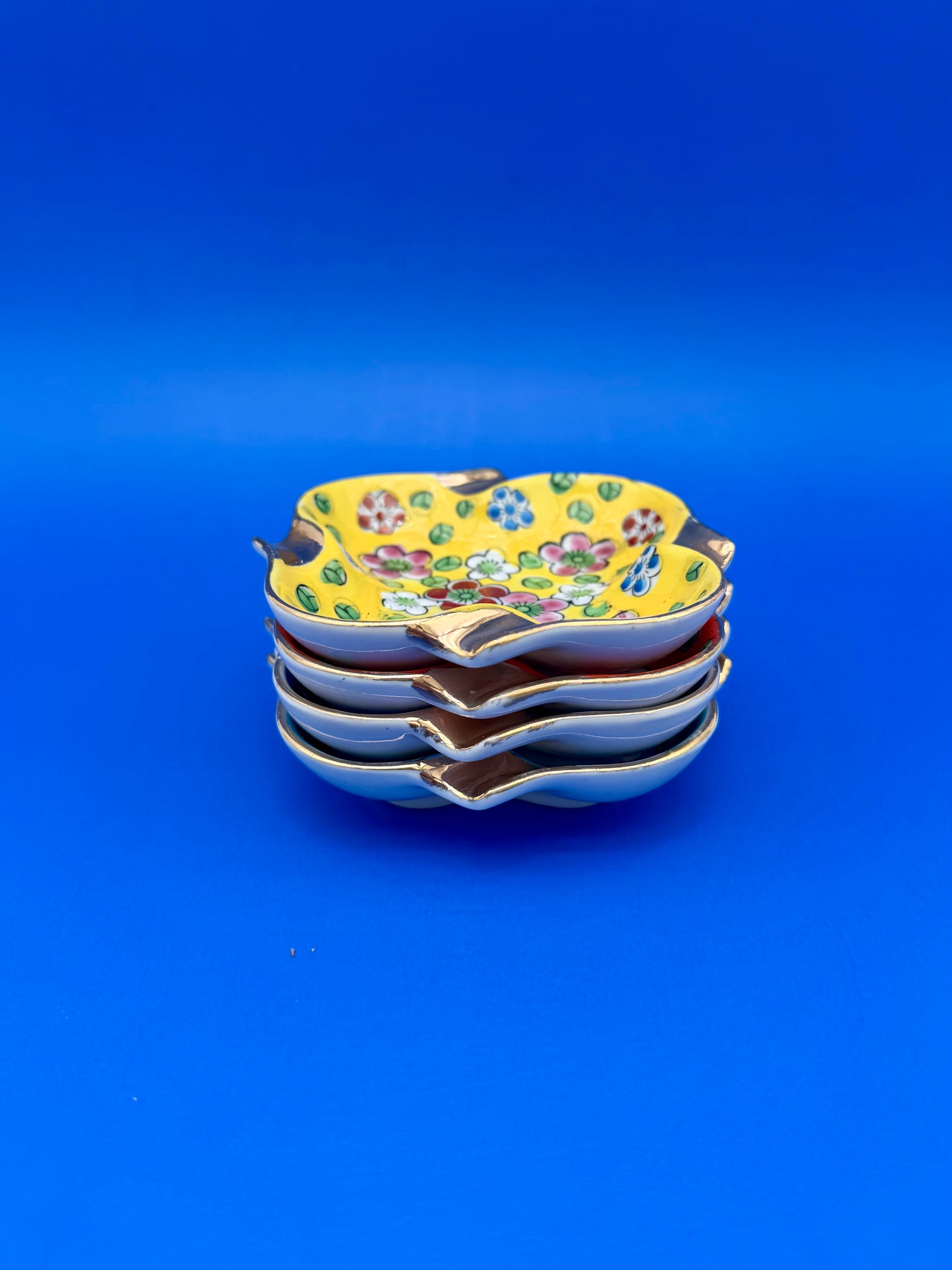 Stack of colorful floral ceramic ashtrays viewed from above, blue background