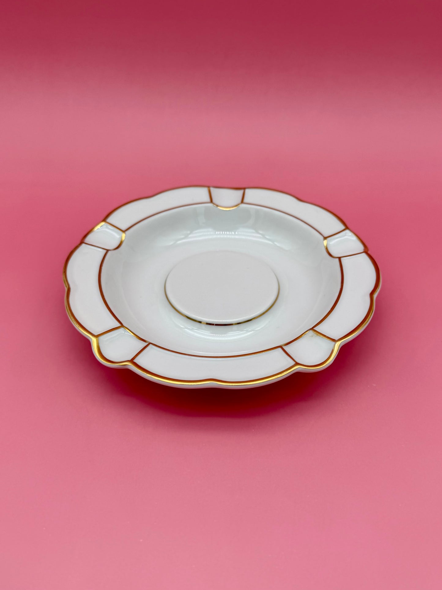 Round white ashtray with paneled scalloped border, shown at a closer angle, pink background