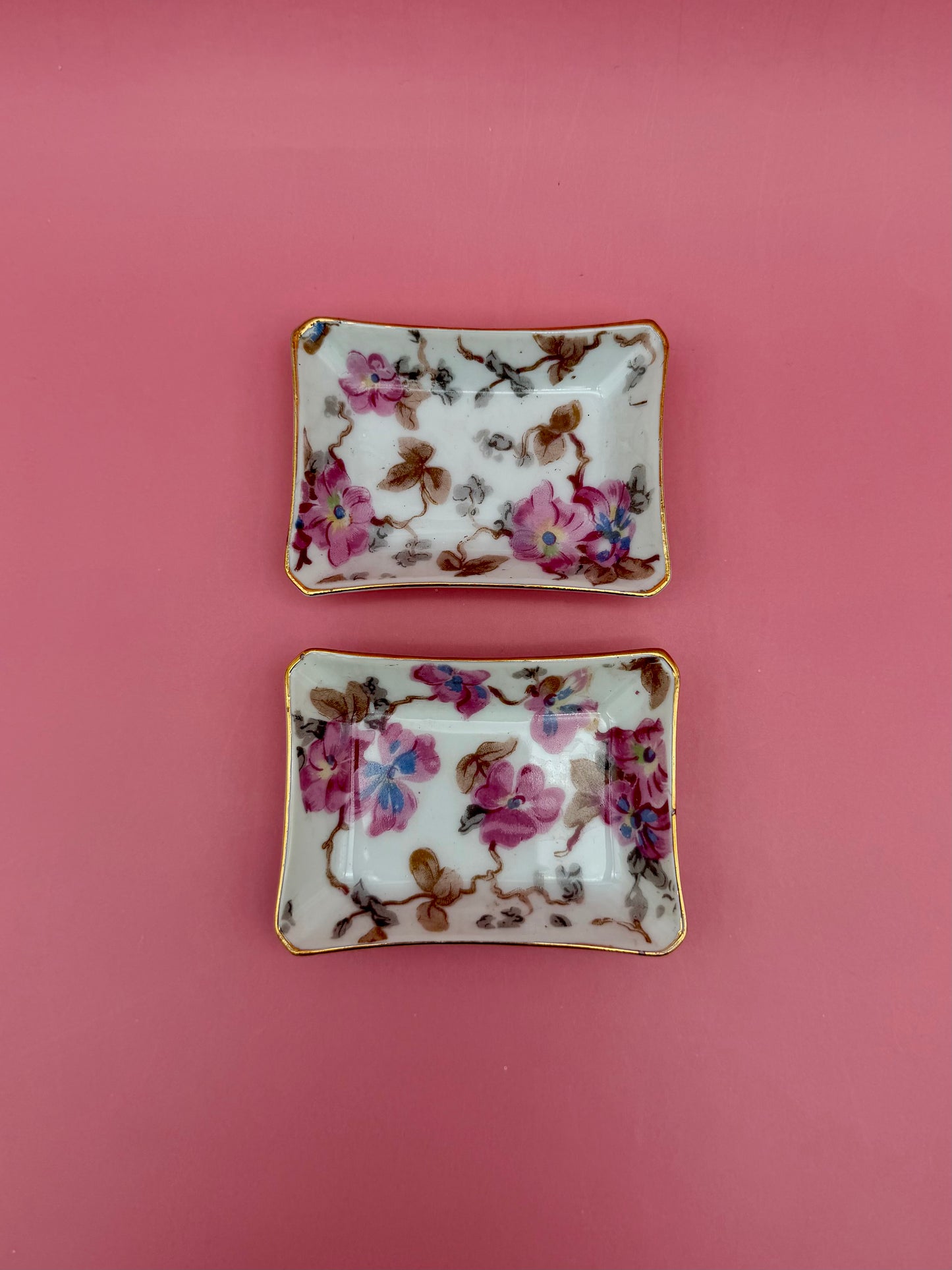 Two floral porcelain ashtrays with pastel flower and leaf design side by side, pink background