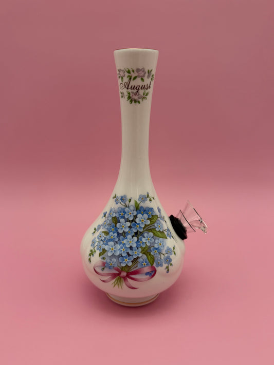 White porcelain bud vase water pipe with blue floral design and gold trim, glass mouthpiece attached at the side, pink background