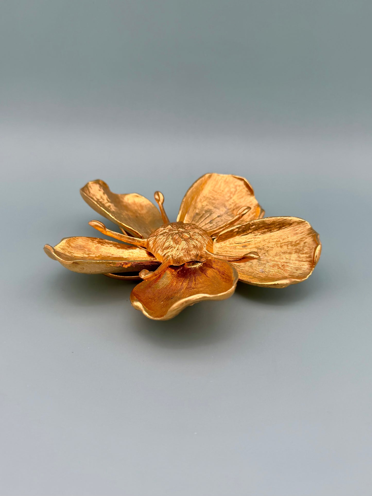 Gold marigold flower-shaped dish shown from an angled side view, showing the cupped petals, gray-blue background.