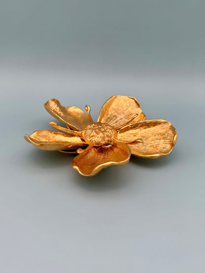 Gold marigold flower-shaped dish shown from an angled side view, showing the cupped petals, gray-blue background.