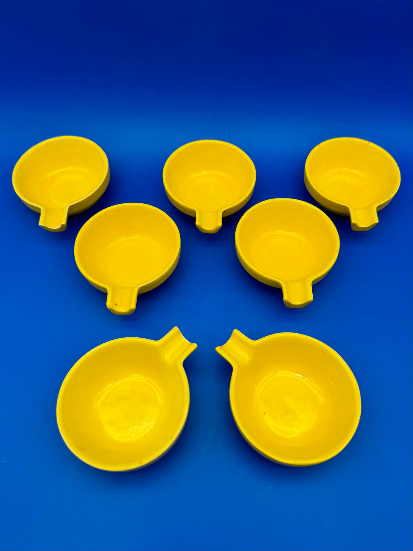 Several round yellow ceramic ashtrays fanned out together, blue background