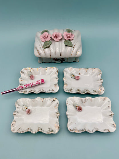 Porcelain stash box topped with dimensional pink roses, surrounded by four matching scalloped mini trays, teal background