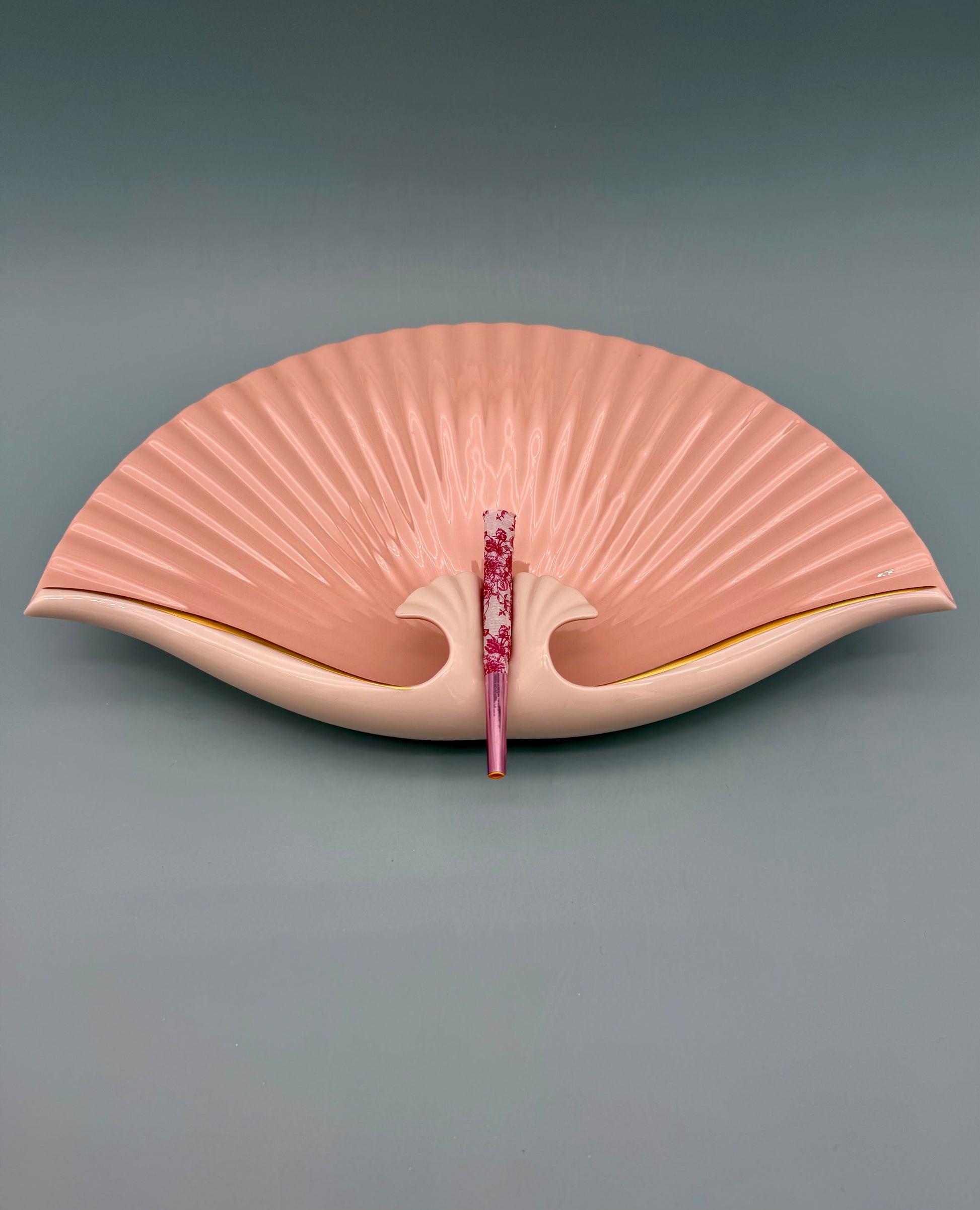 Blush pink seashell-shaped porcelain ashtray with fan-like ridges and a gold rim, gray background