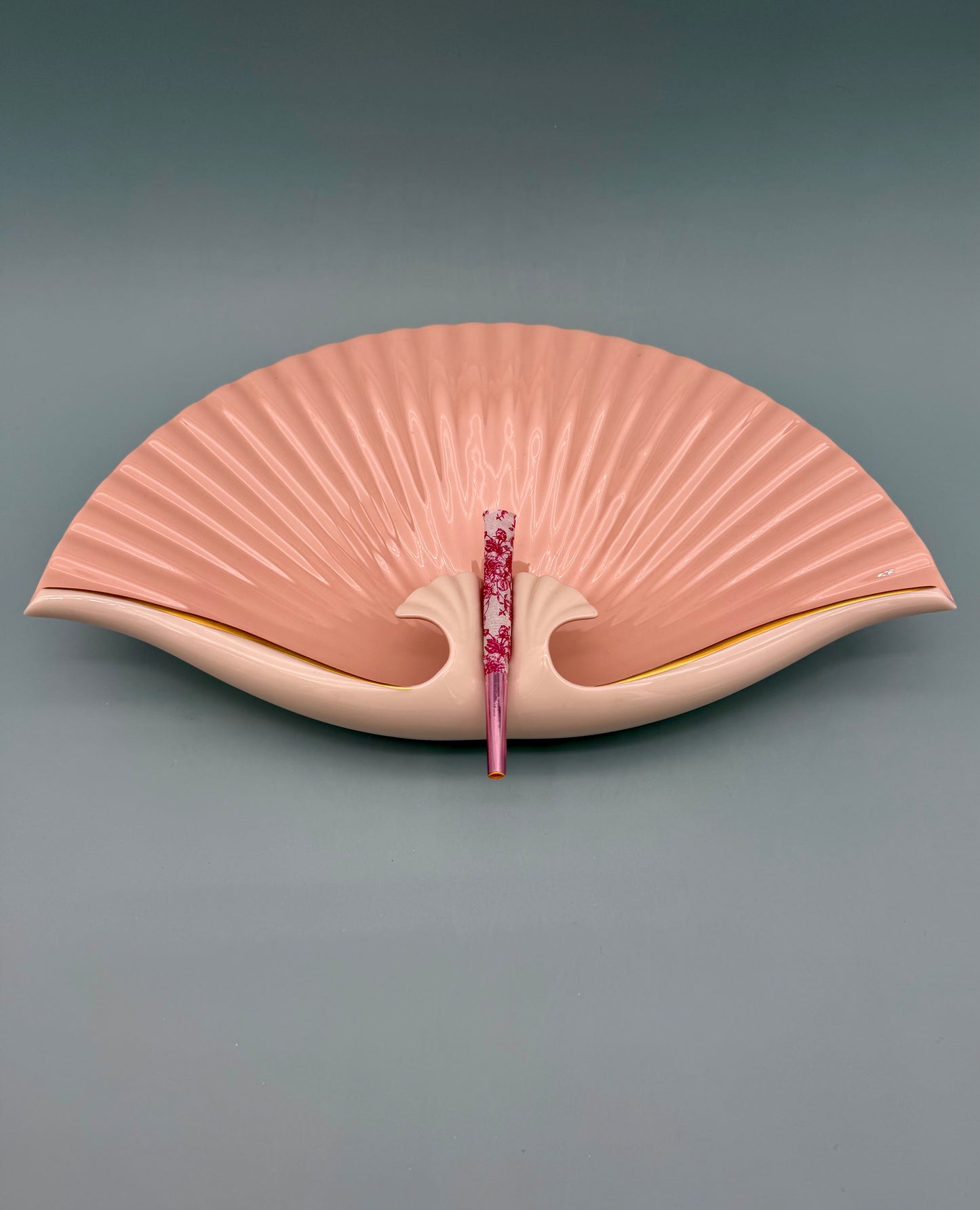 Blush pink seashell-shaped porcelain ashtray with fan-like ridges and a gold rim, gray background