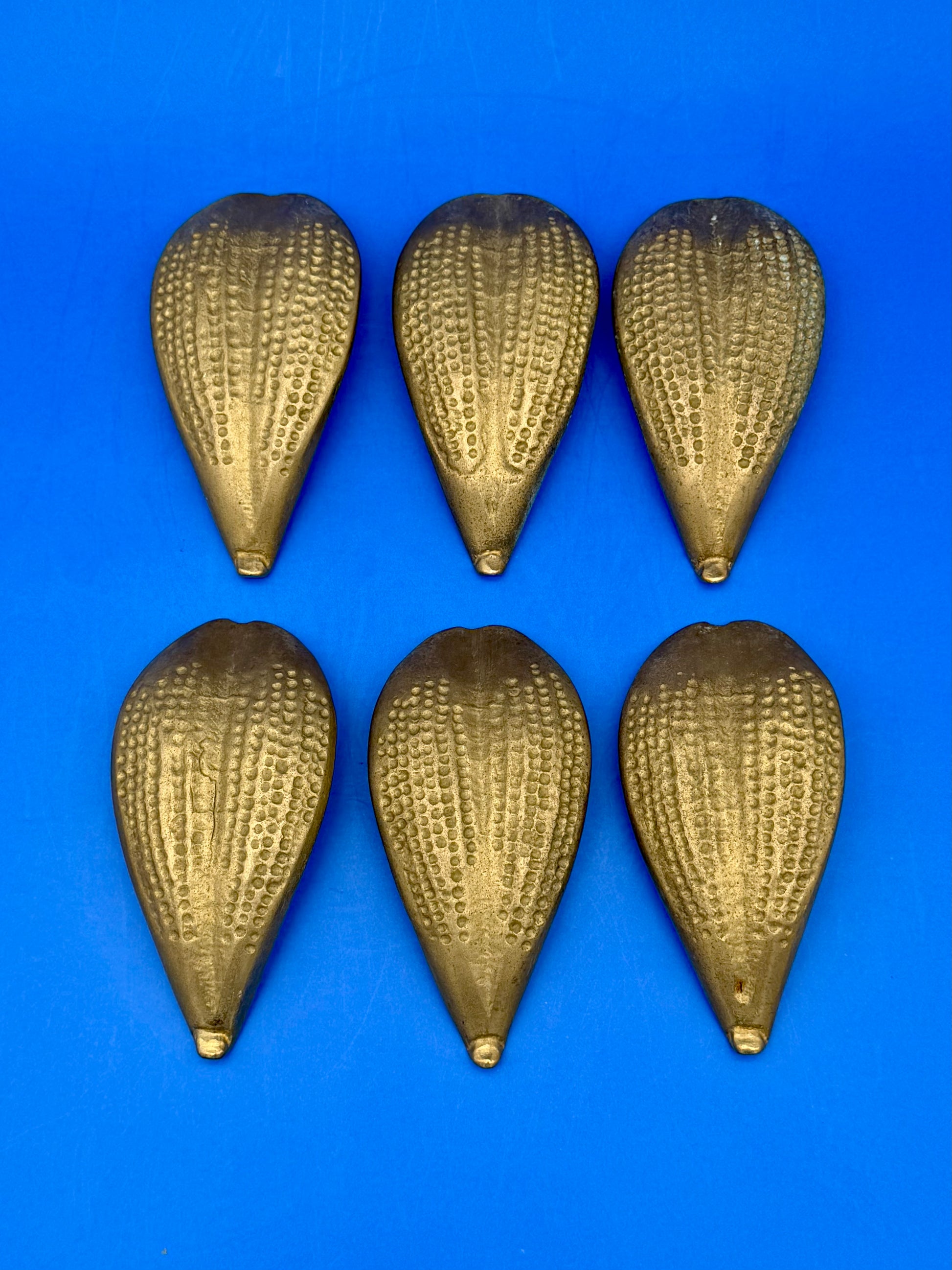 Six brass leaf-shaped petal ashtrays arranged in two rows, blue background
