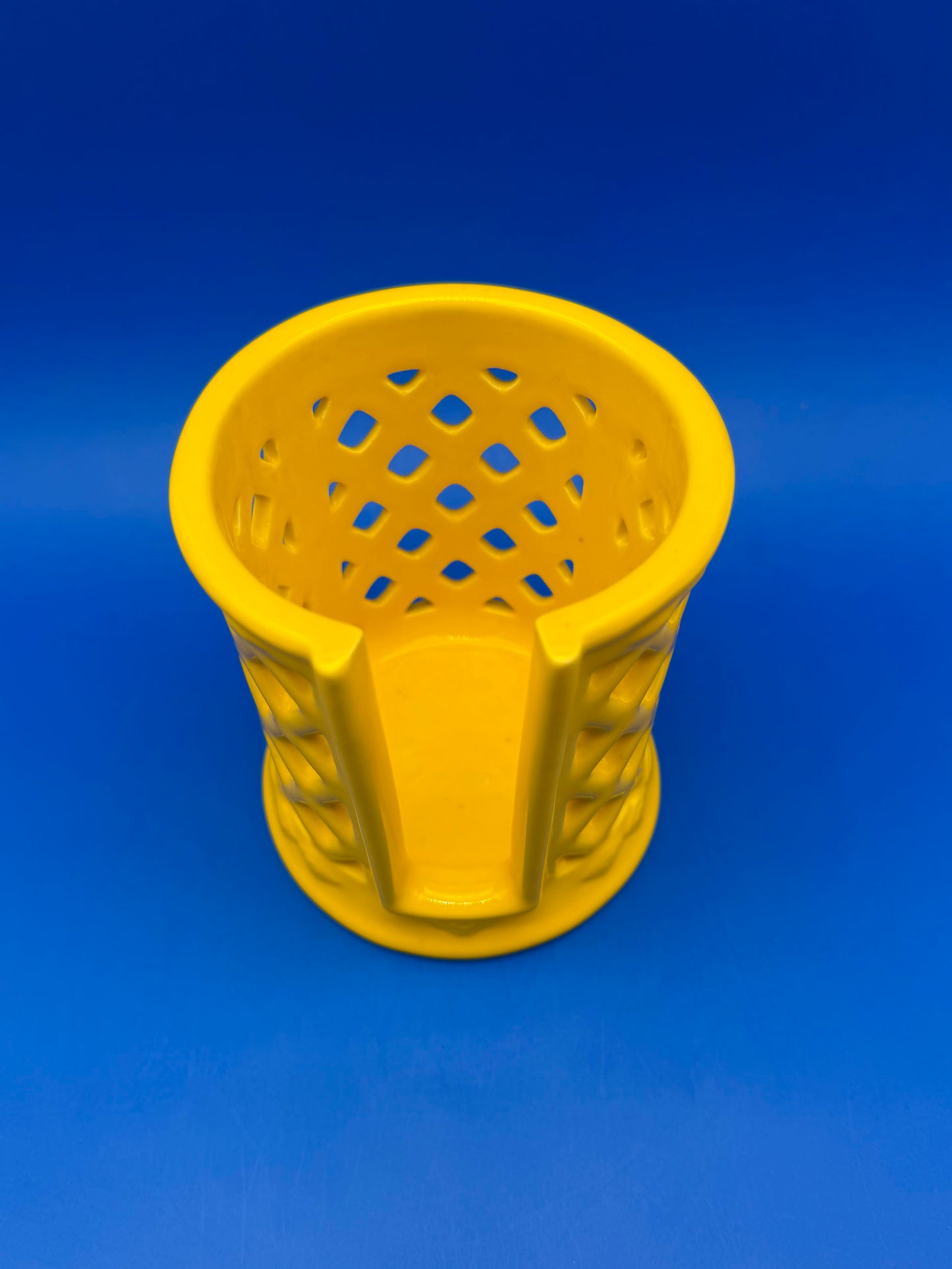 Yellow ceramic lattice ashtray holder with scalloped rim showing woven basket-style cutouts, blue background