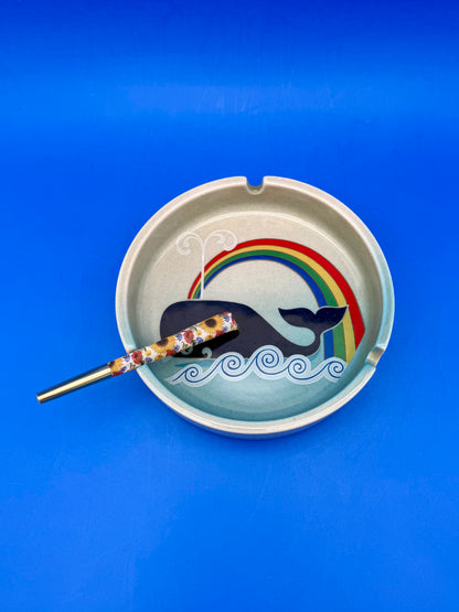 Whale and rainbow ashtray with a floral-patterned cigarette pick resting inside, blue background