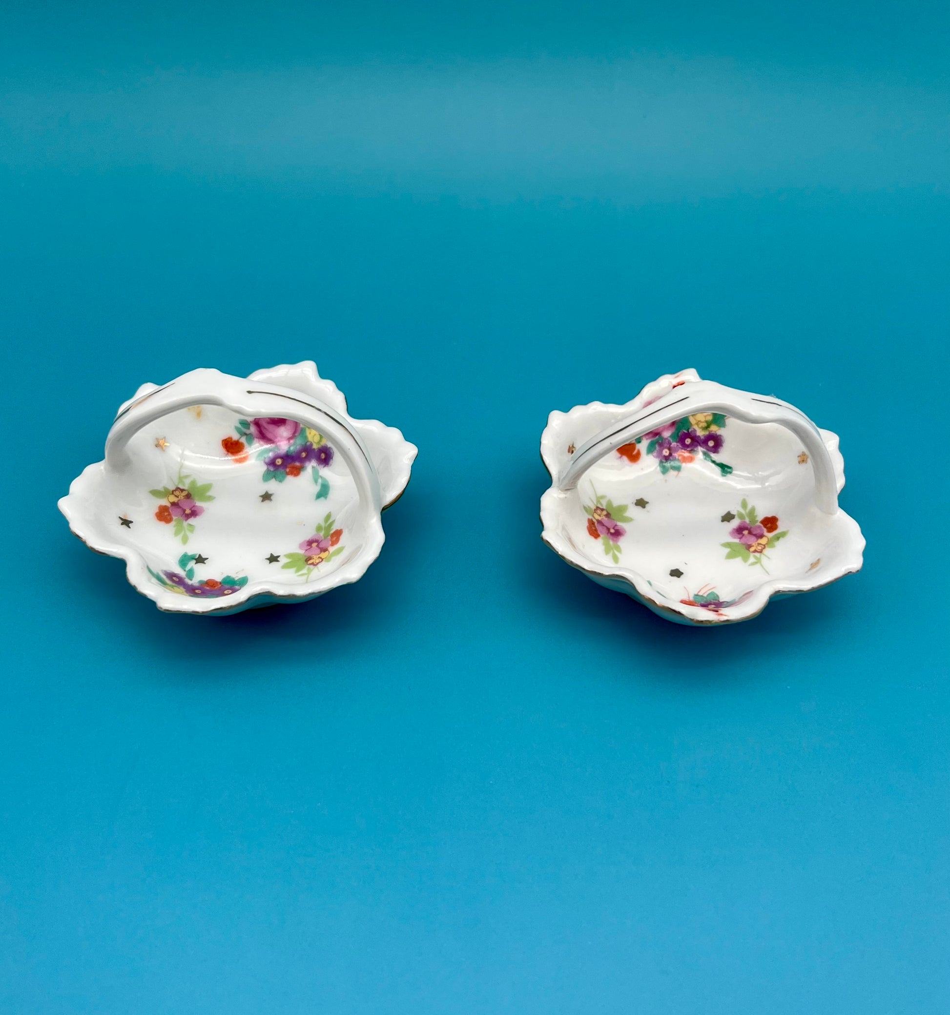 Angled view of the two Reagan Set porcelain ashtrays showing their scalloped shape and floral gold-star design, teal background.