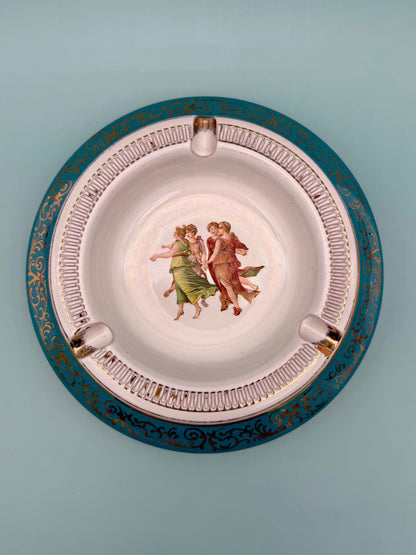 Round turquoise porcelain ashtray with a dancing figures medallion and ornate gold scrollwork, gray background