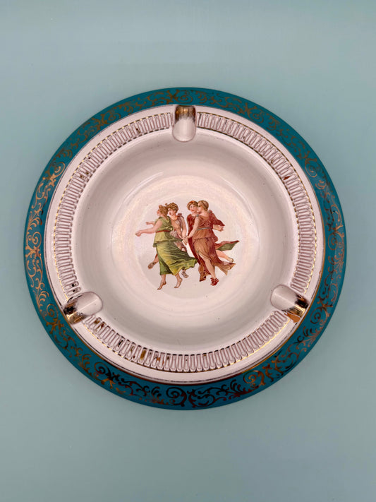 Round turquoise porcelain ashtray with a dancing figures medallion and ornate gold scrollwork, gray background