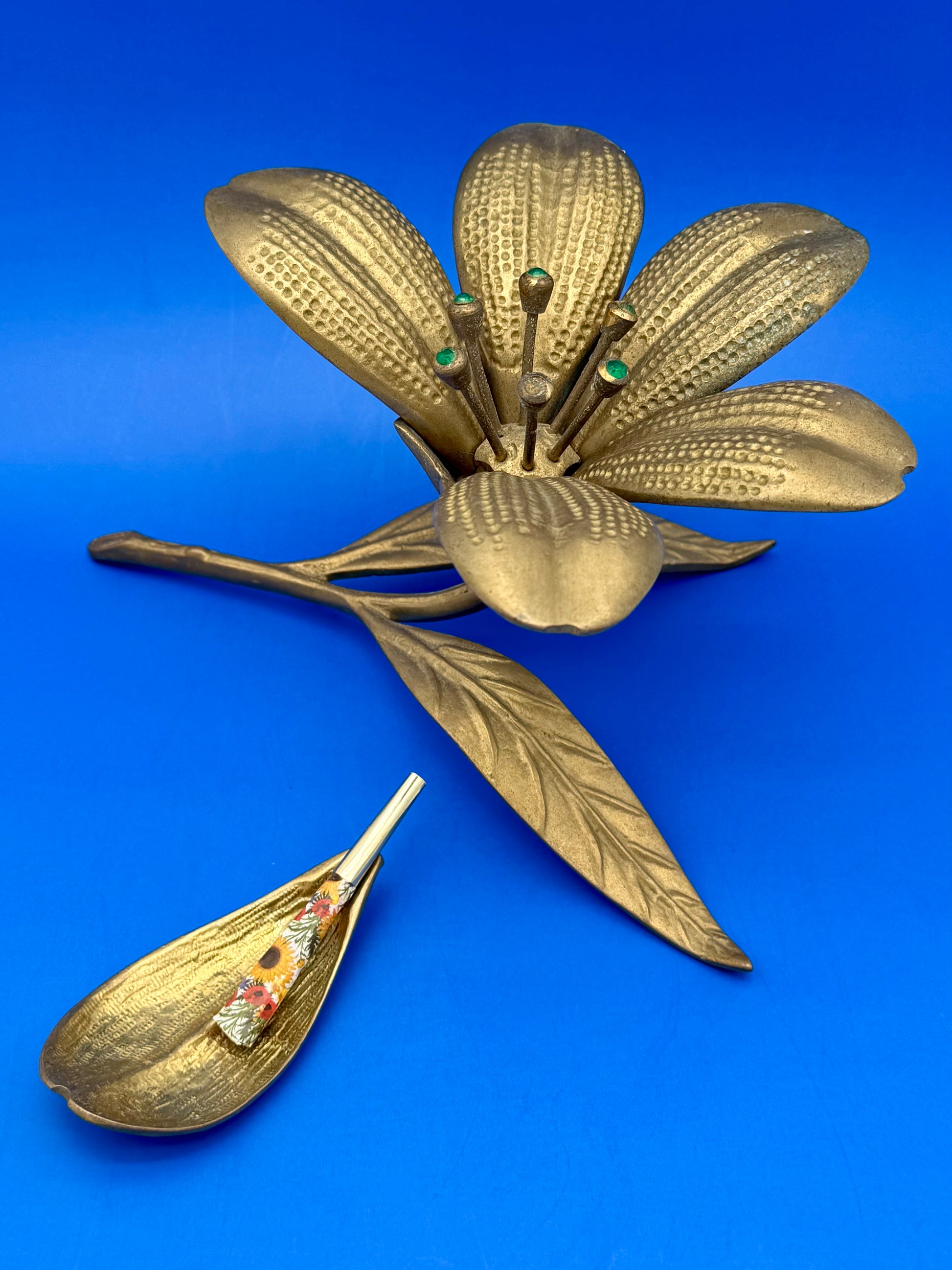 Close-up of the brass flower ashtray's center with green jewel accents, a removable petal ashtray resting beside it
