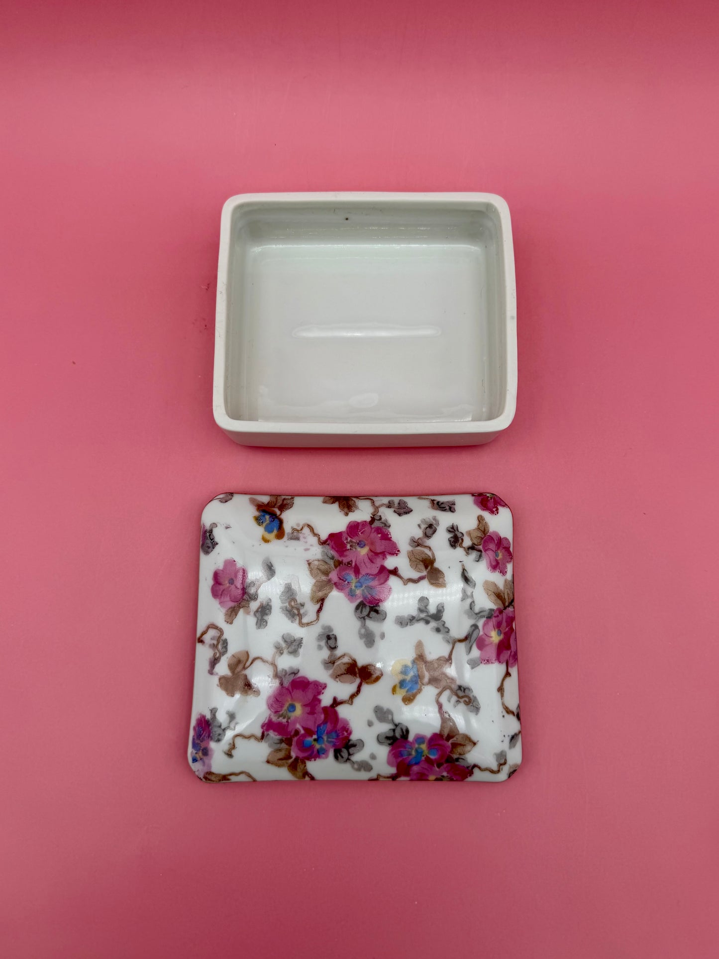 Open empty porcelain stash box beside its floral-painted lid, pink background