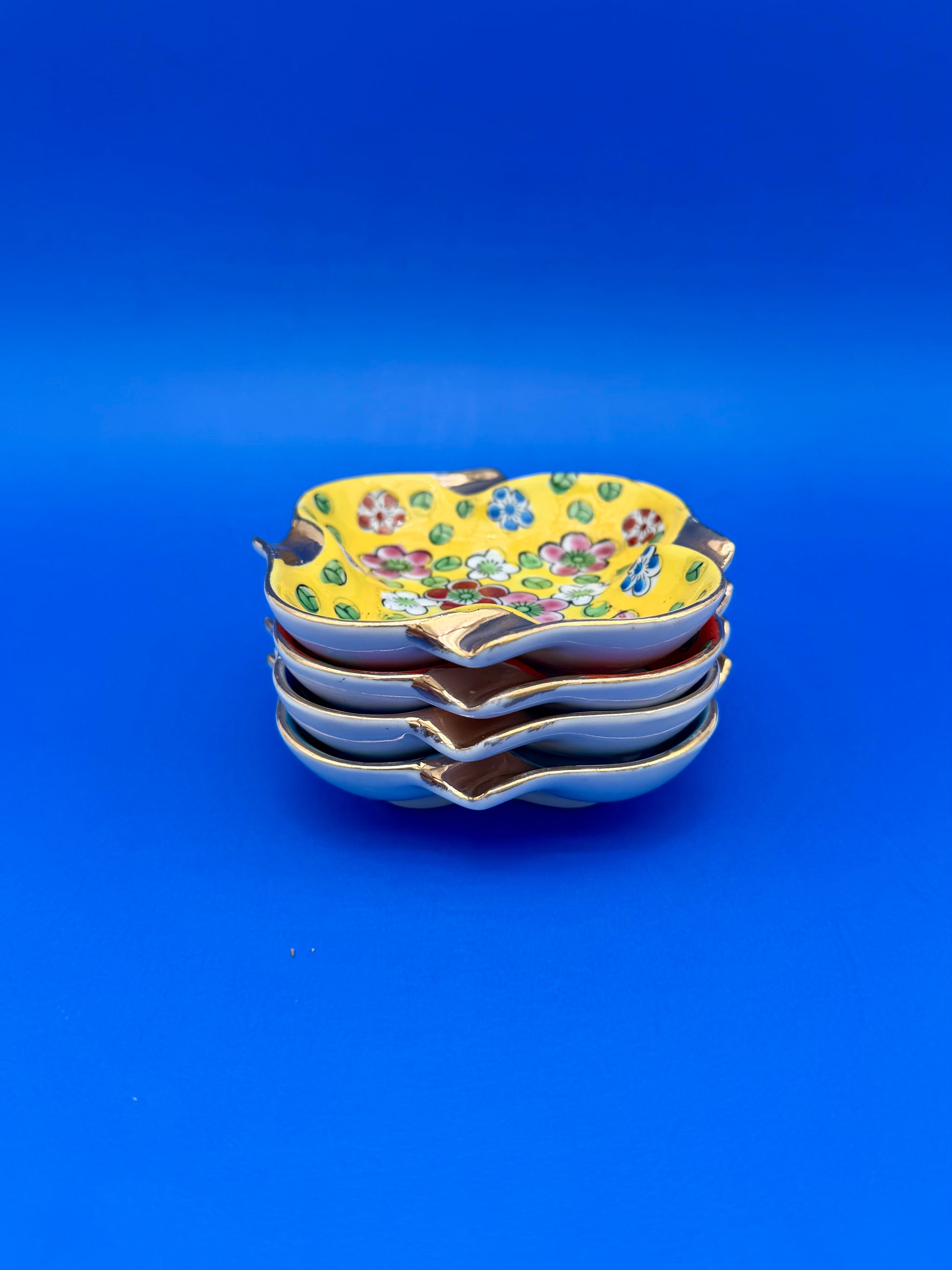 Stack of colorful floral ceramic ashtrays viewed from above, blue background