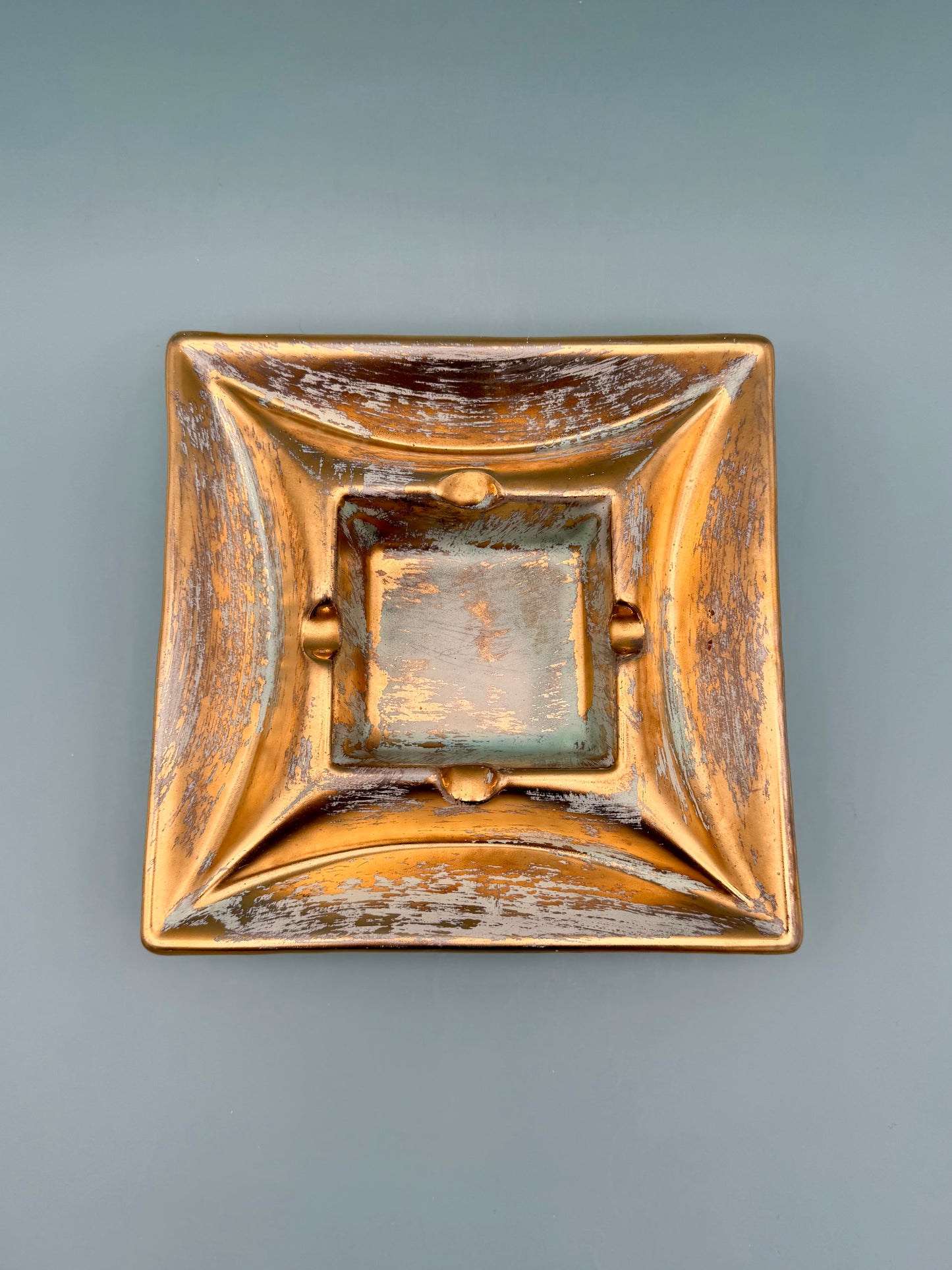 Square gold and copper pottery ashtray viewed from above, gray background