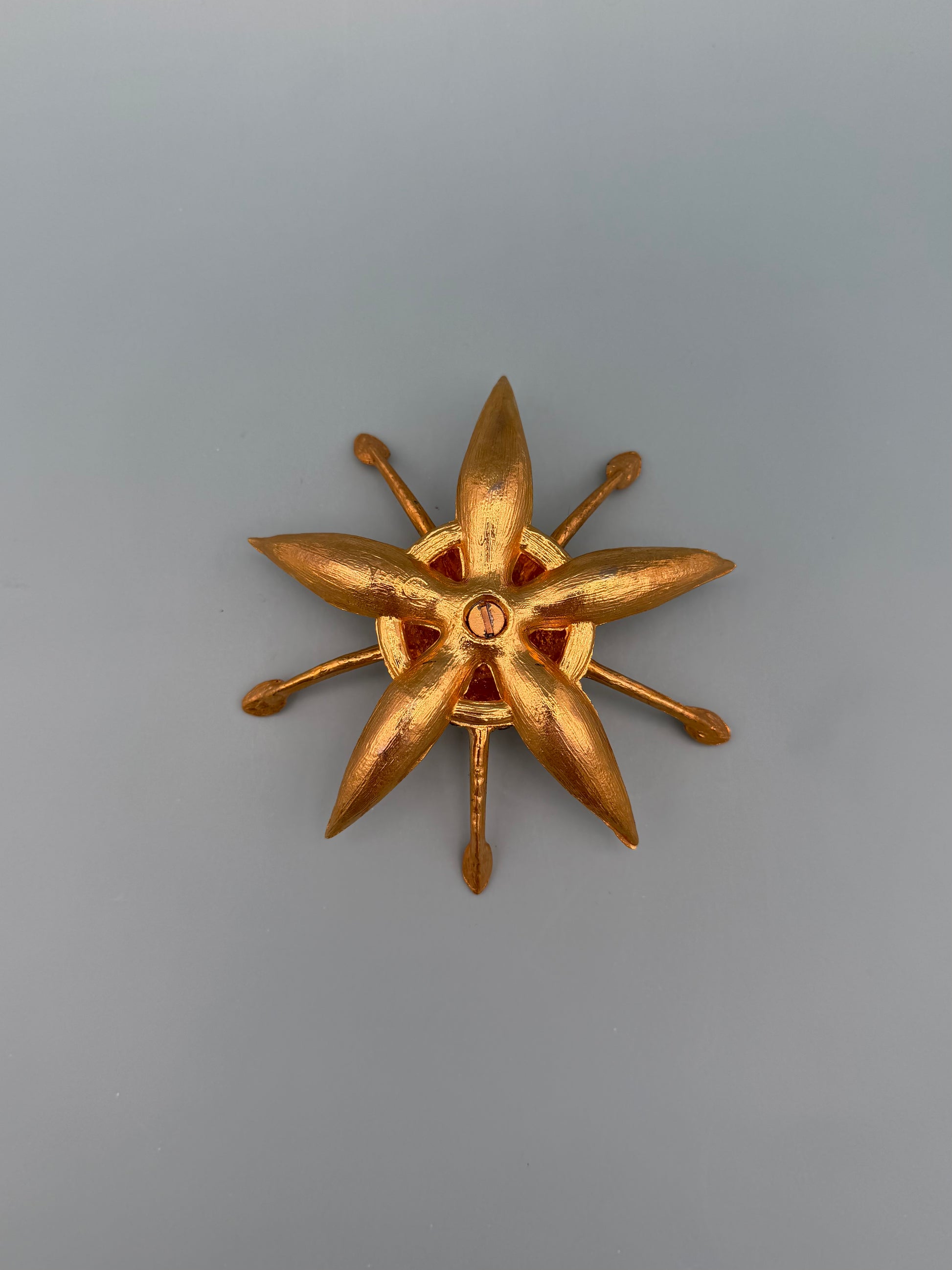 Similar gold starburst-shaped dish with pointed rays and a small red jeweled center accent, gray-blue background.