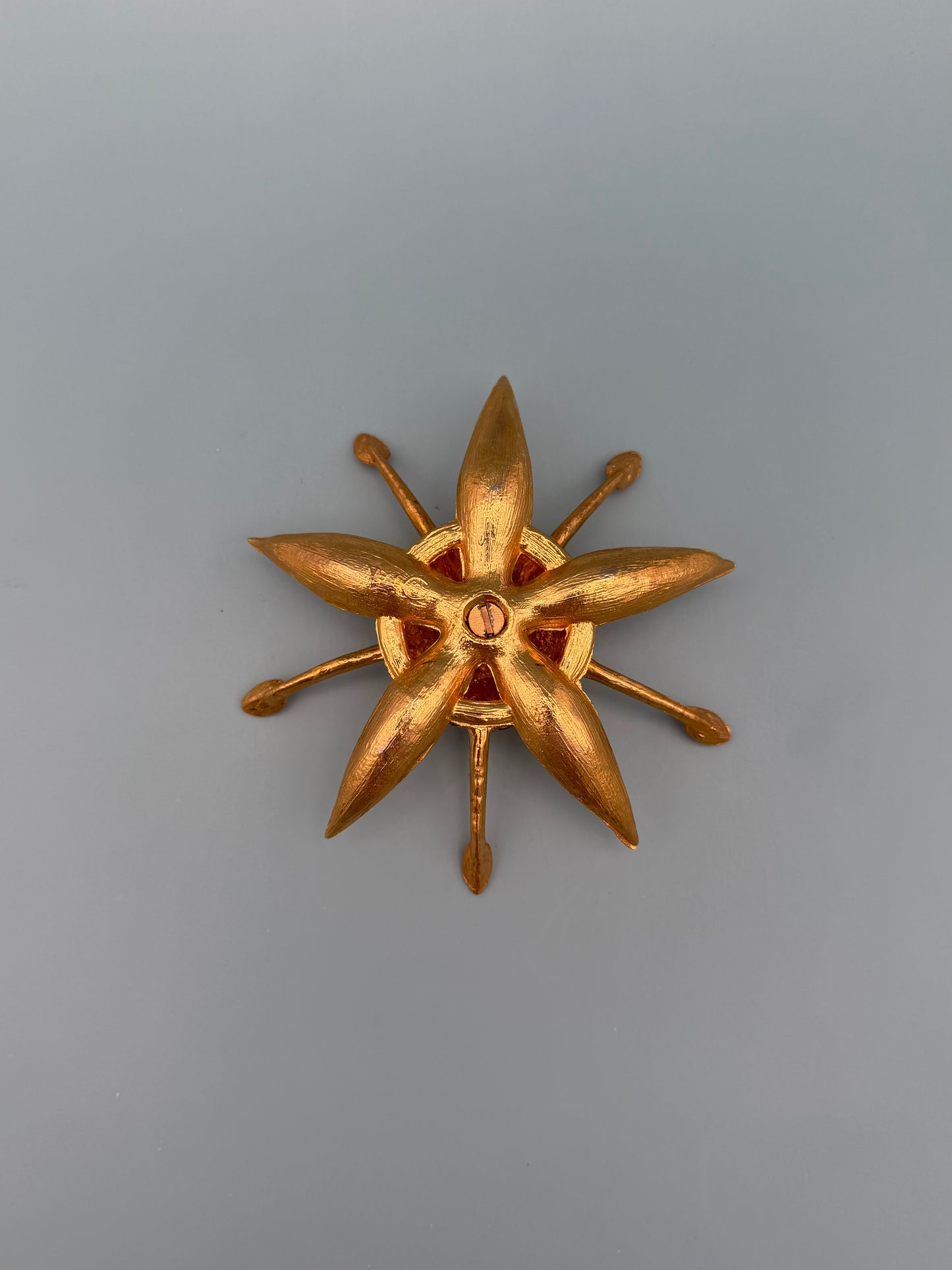Similar gold starburst-shaped dish with pointed rays and a small red jeweled center accent, gray-blue background.