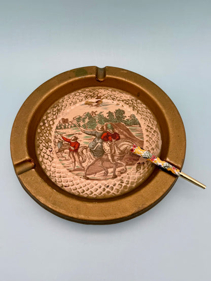 Round Florentine ashtray with hand-painted horseback rider landscape scene and gold toned frame, with a cigarette pick, gray background