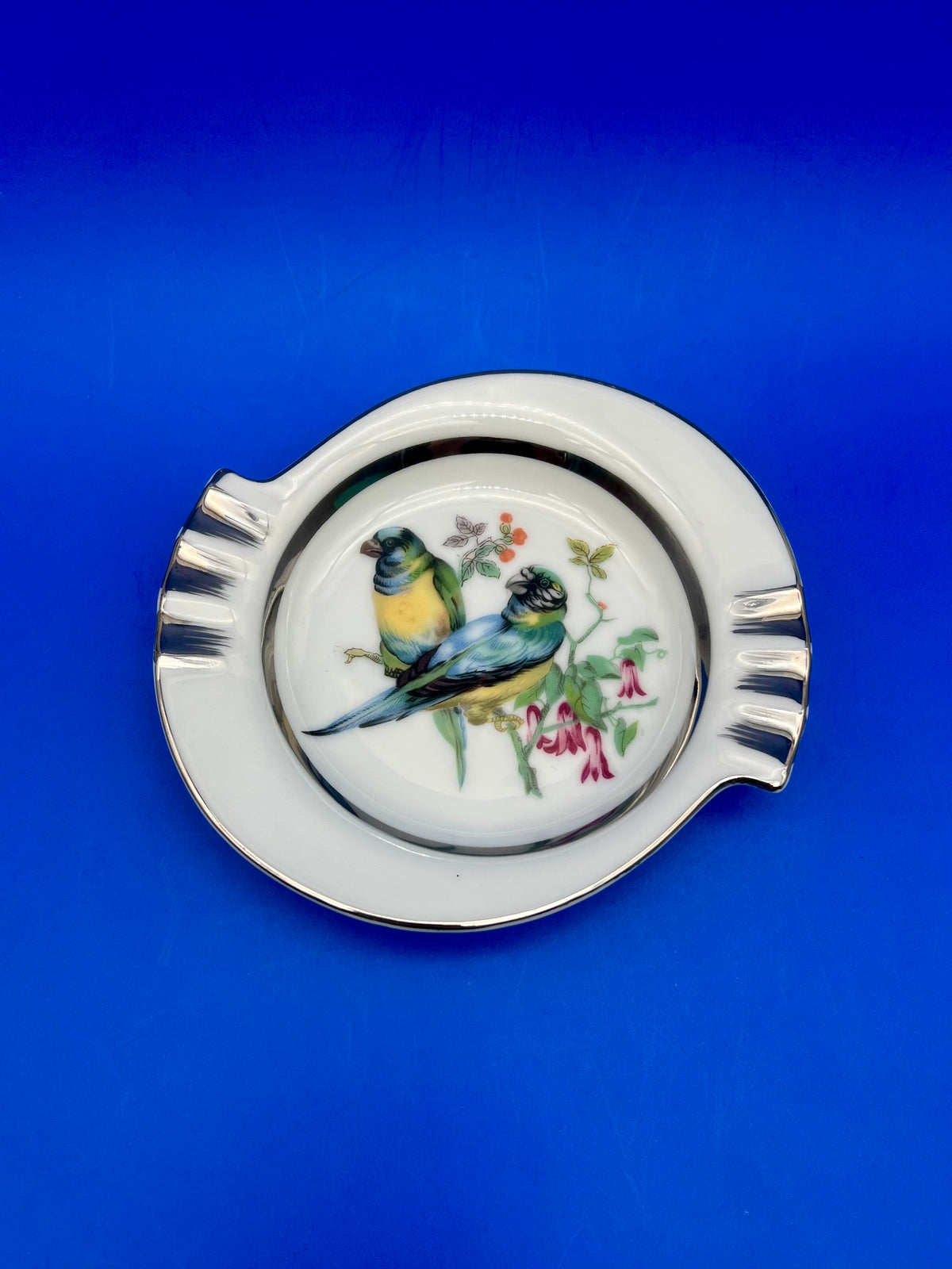 Round white ceramic ashtray featuring a painted bird design on a blue background
