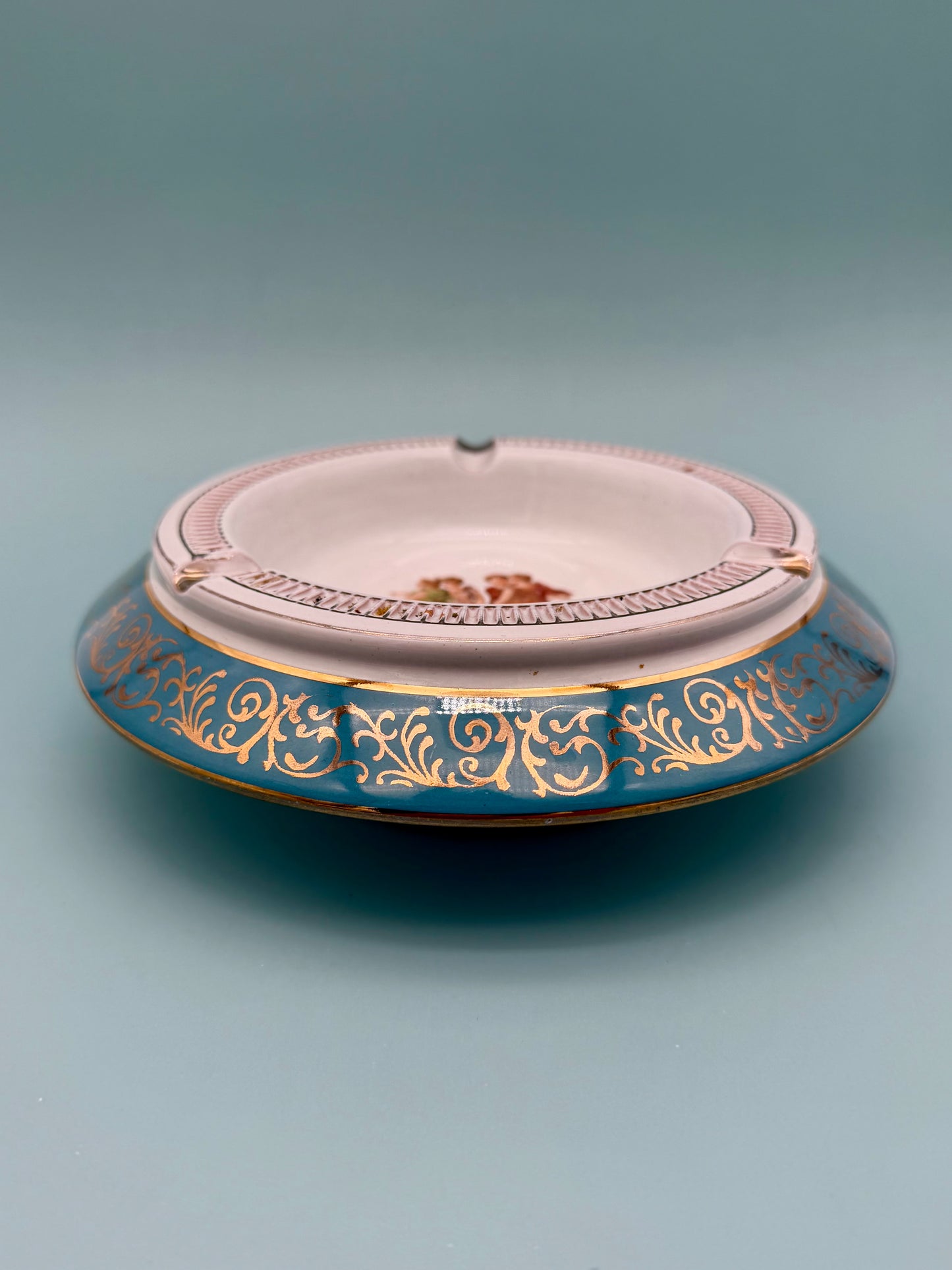 Turquoise and gold dancing figures ashtray shown from a side profile, gray background