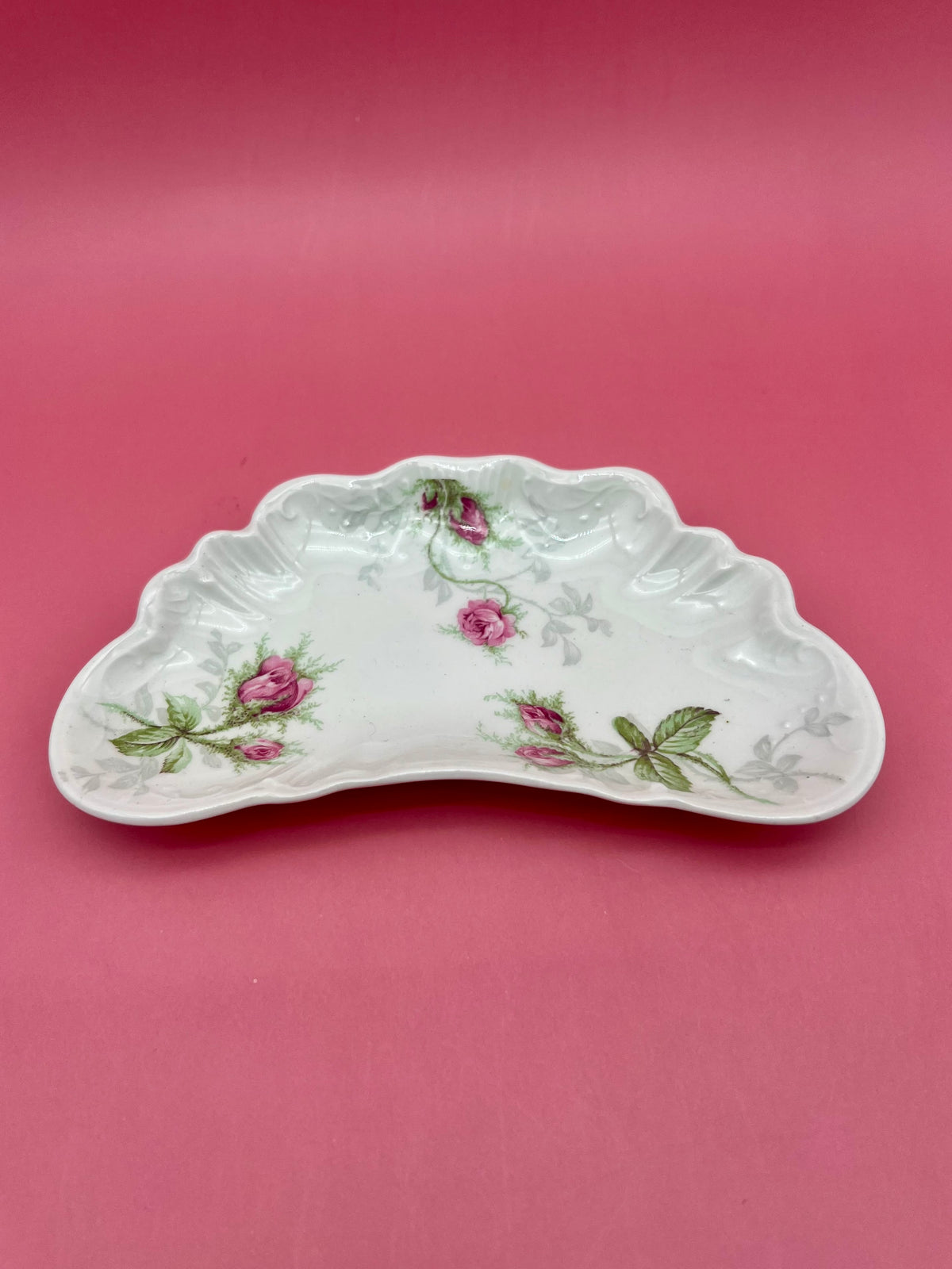 Close-up of the crescent-shaped Madison ashtray showing its scalloped edges and pink floral design, pink background.