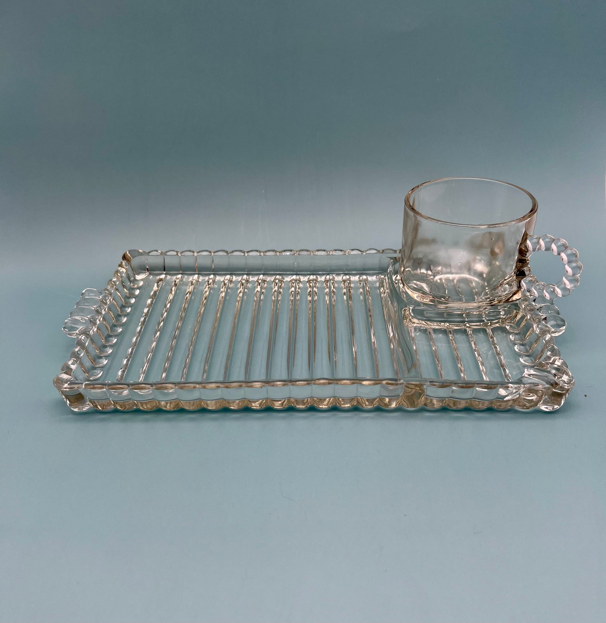 Angled view of the Hazel Set pressed glass tray and matching mug showing the geometric ribbed pattern, gray background.