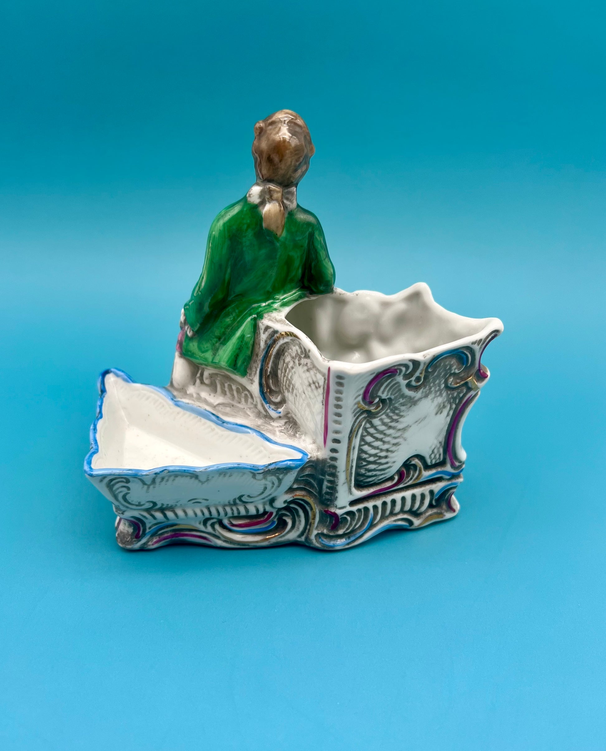 Front-angled view of the Ludwig Set figurine and its scrollwork ashtray holder base, teal background.