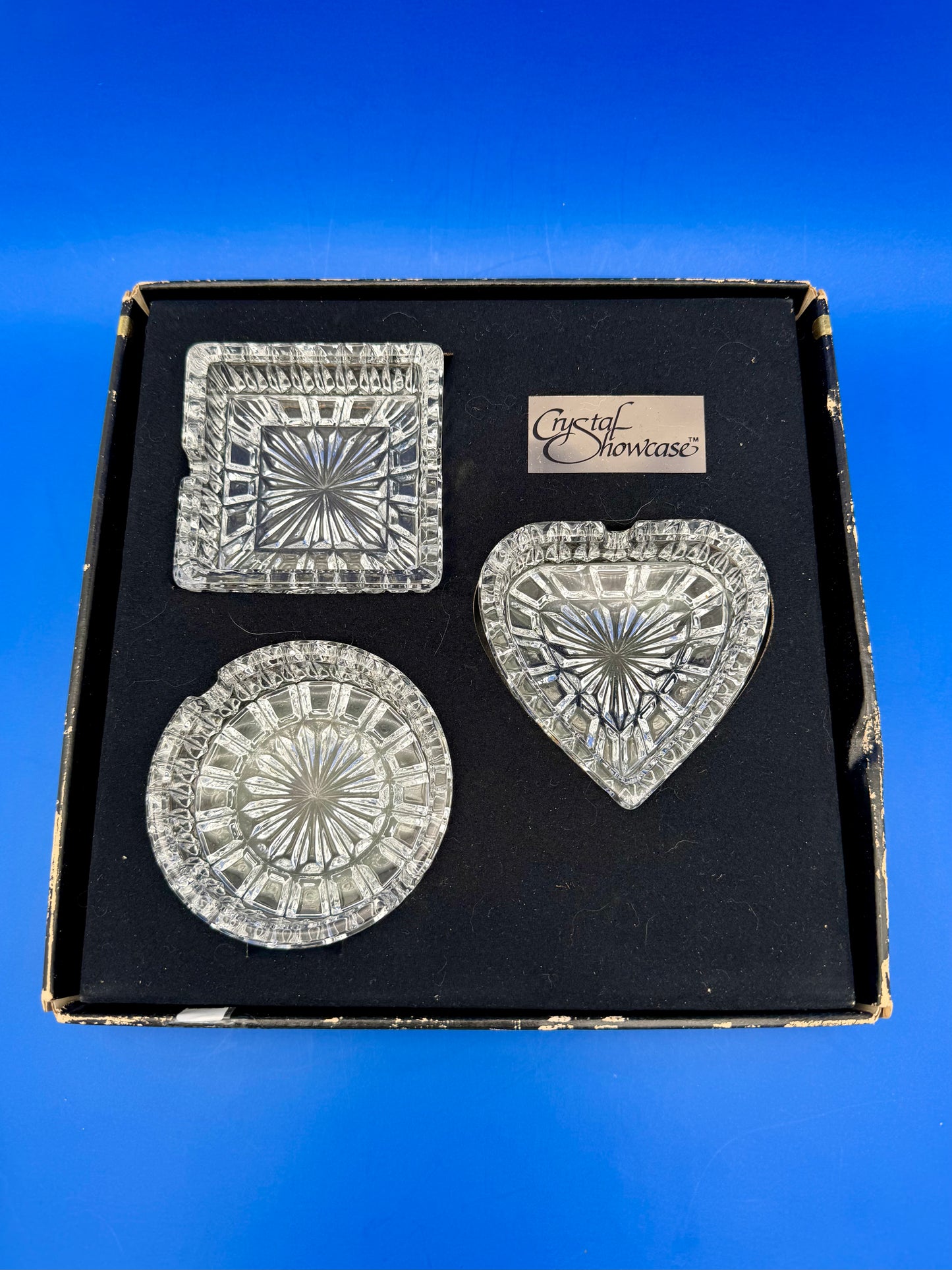Boxed vintage crystal ashtray set with square, round, and heart-shaped faceted glass dishes nested in their original box, blue background