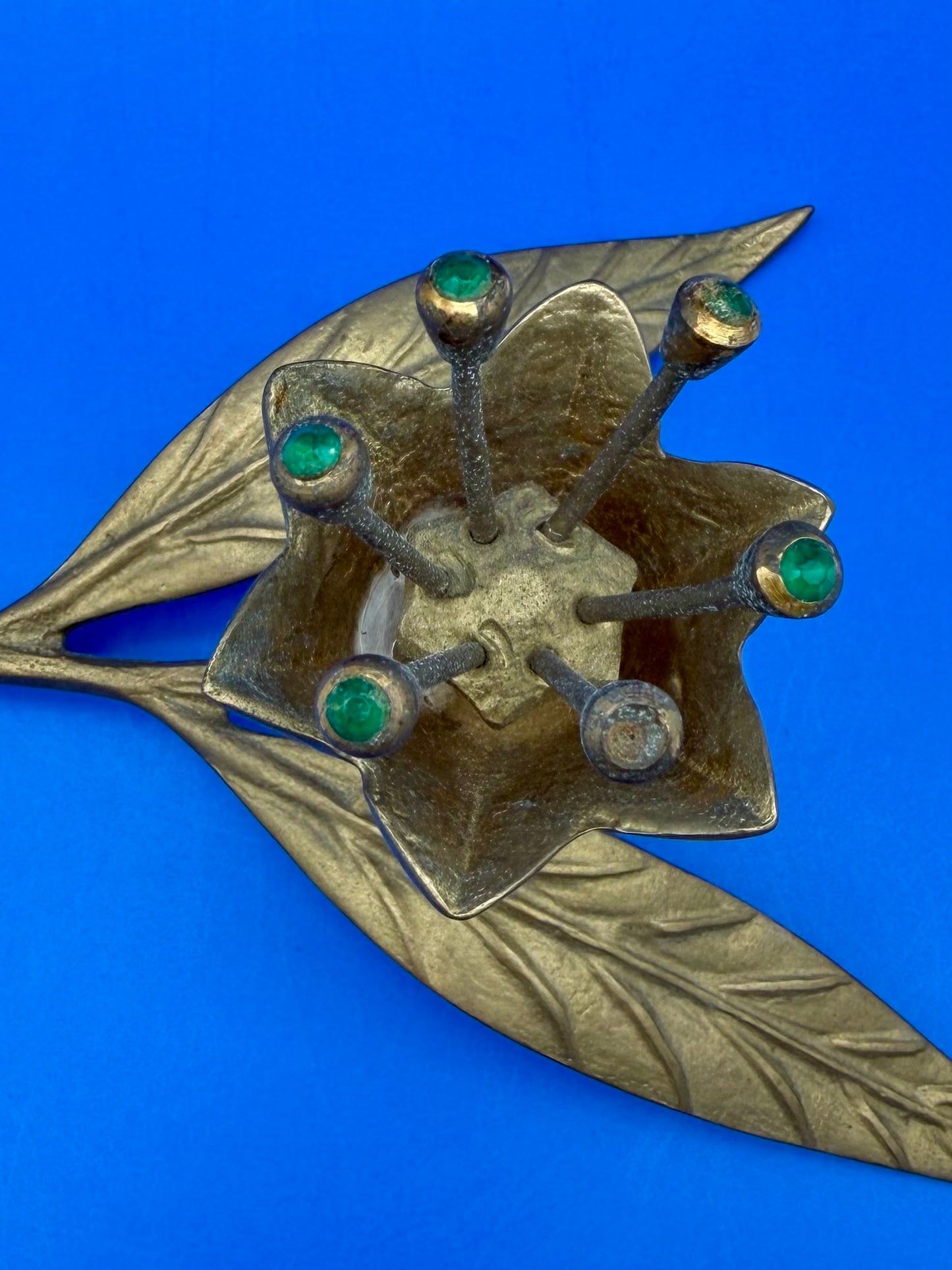 Close-up of the brass flower ashtray's center cluster showing green and clear jewel accents, blue background