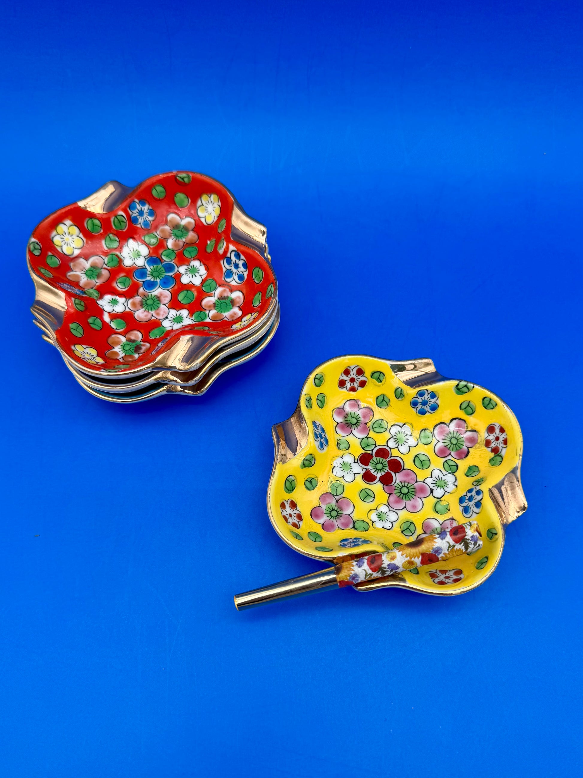 Stack of colorful floral ceramic ashtrays with one holding a glass cigarette pick, blue background