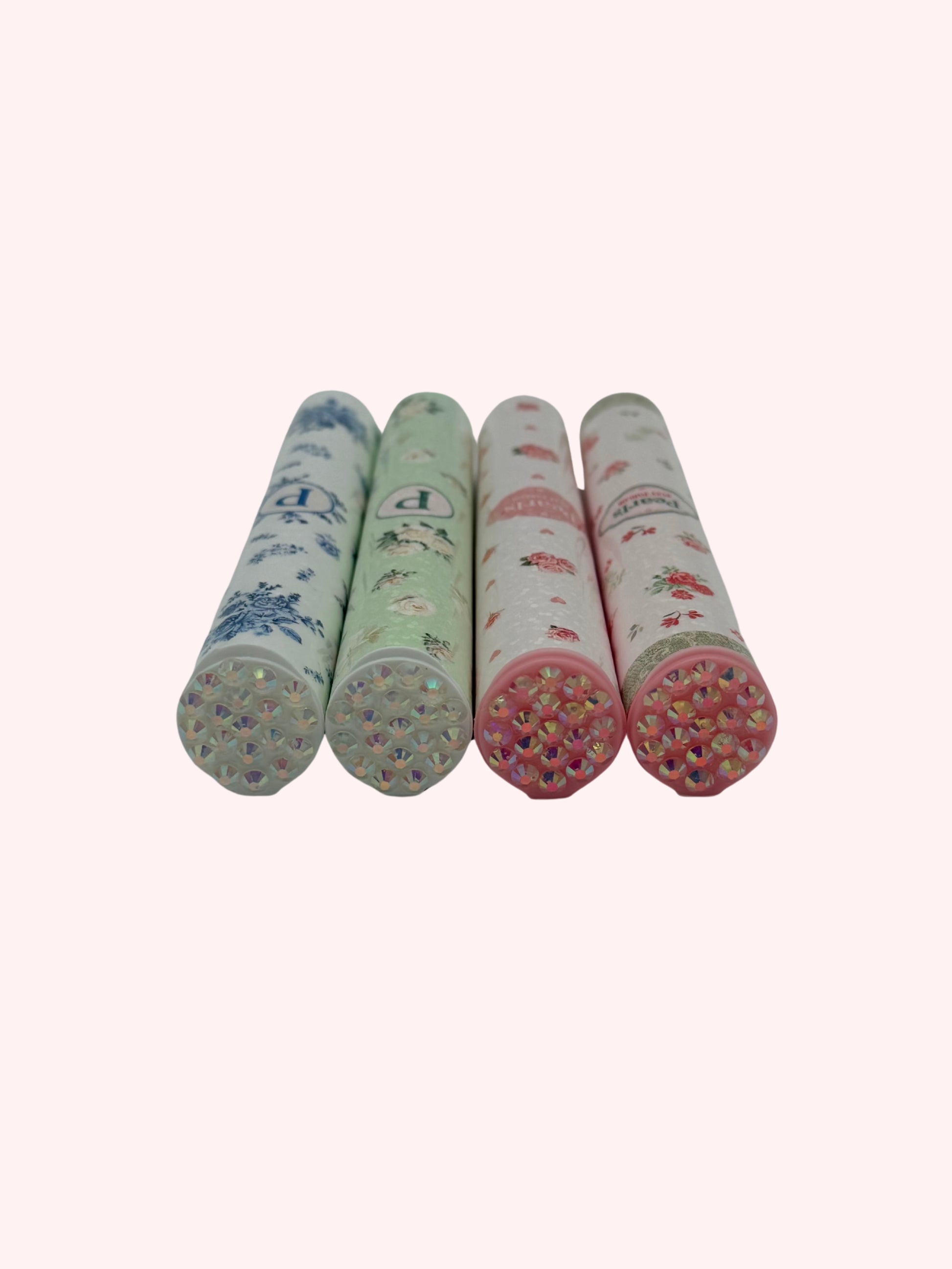 Close-up of four doob tube rhinestone lids in mint, blue, and pink floral designs, laid on their sides