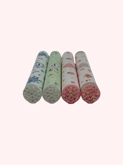 Close-up of four doob tube rhinestone lids in mint, blue, and pink floral designs, laid on their sides