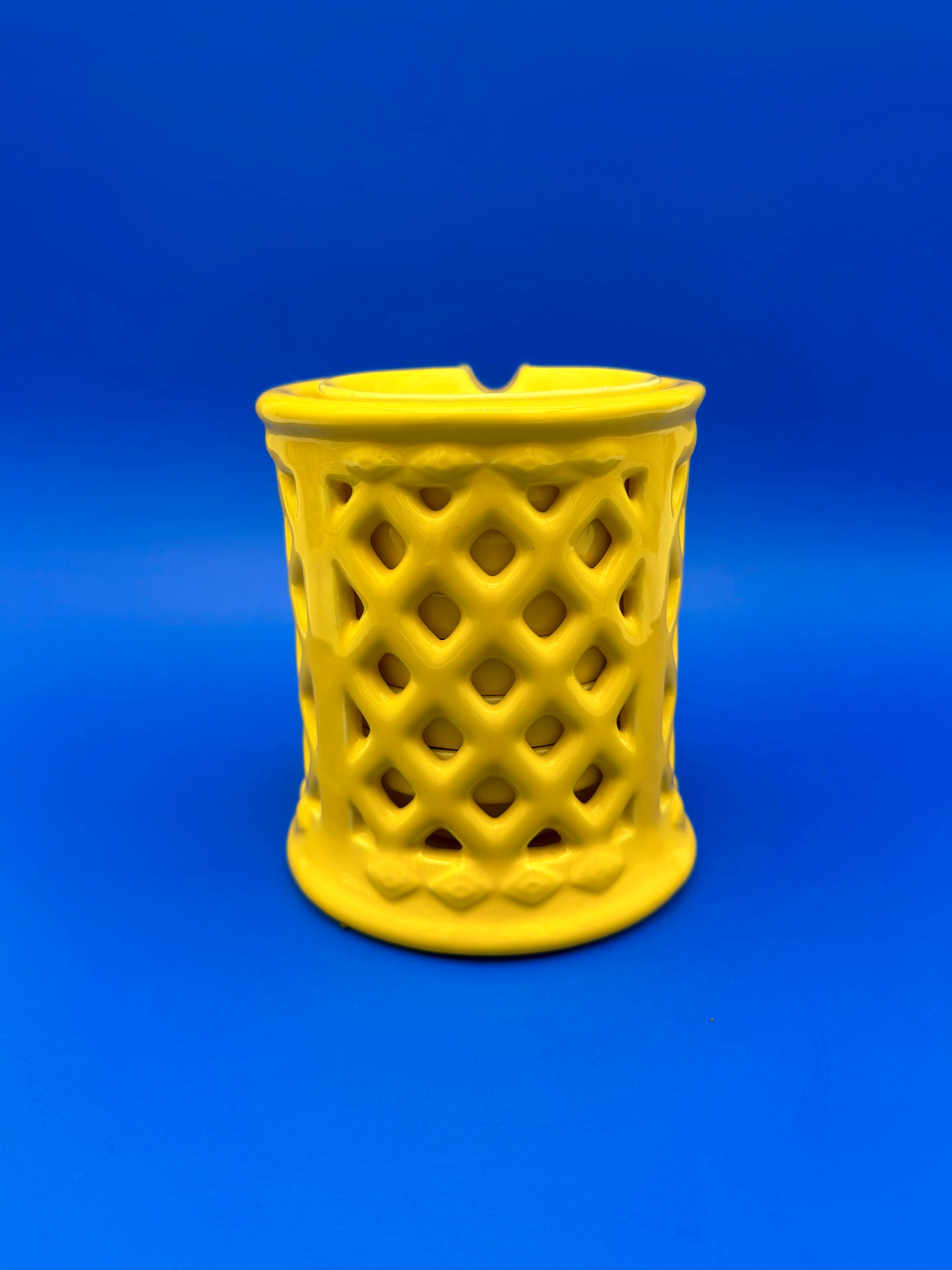 Yellow ceramic lattice ashtray holder shown from a different angle with a diamond cutout pattern, blue background