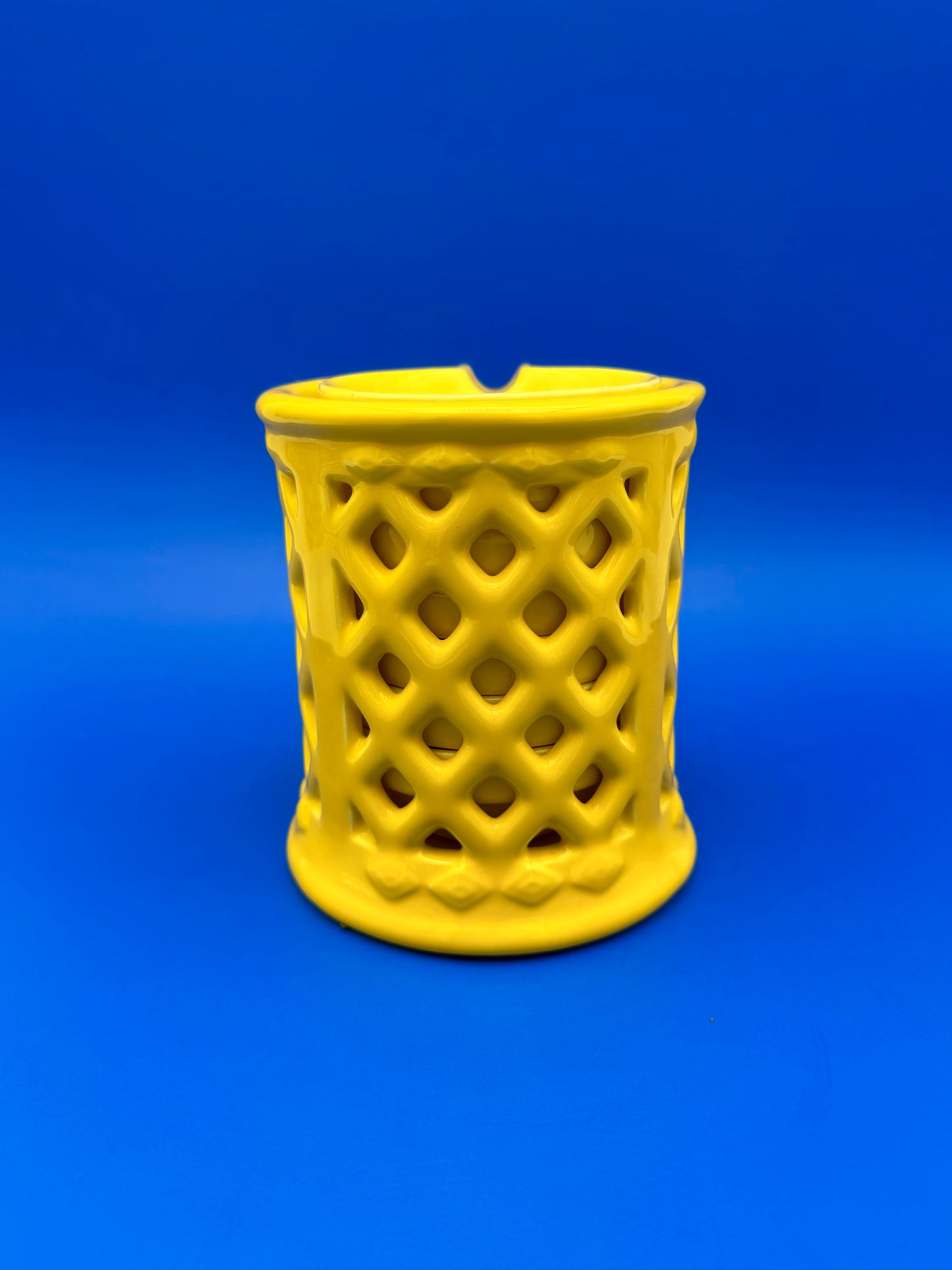 Yellow ceramic lattice ashtray holder shown from a different angle with a diamond cutout pattern, blue background