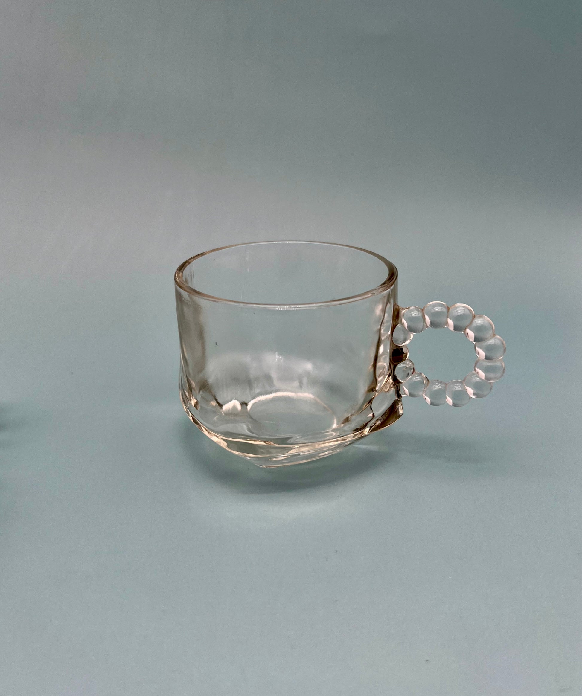 Single pressed glass mug from the Hazel Set with a ribbed pattern and curved handle, gray background.