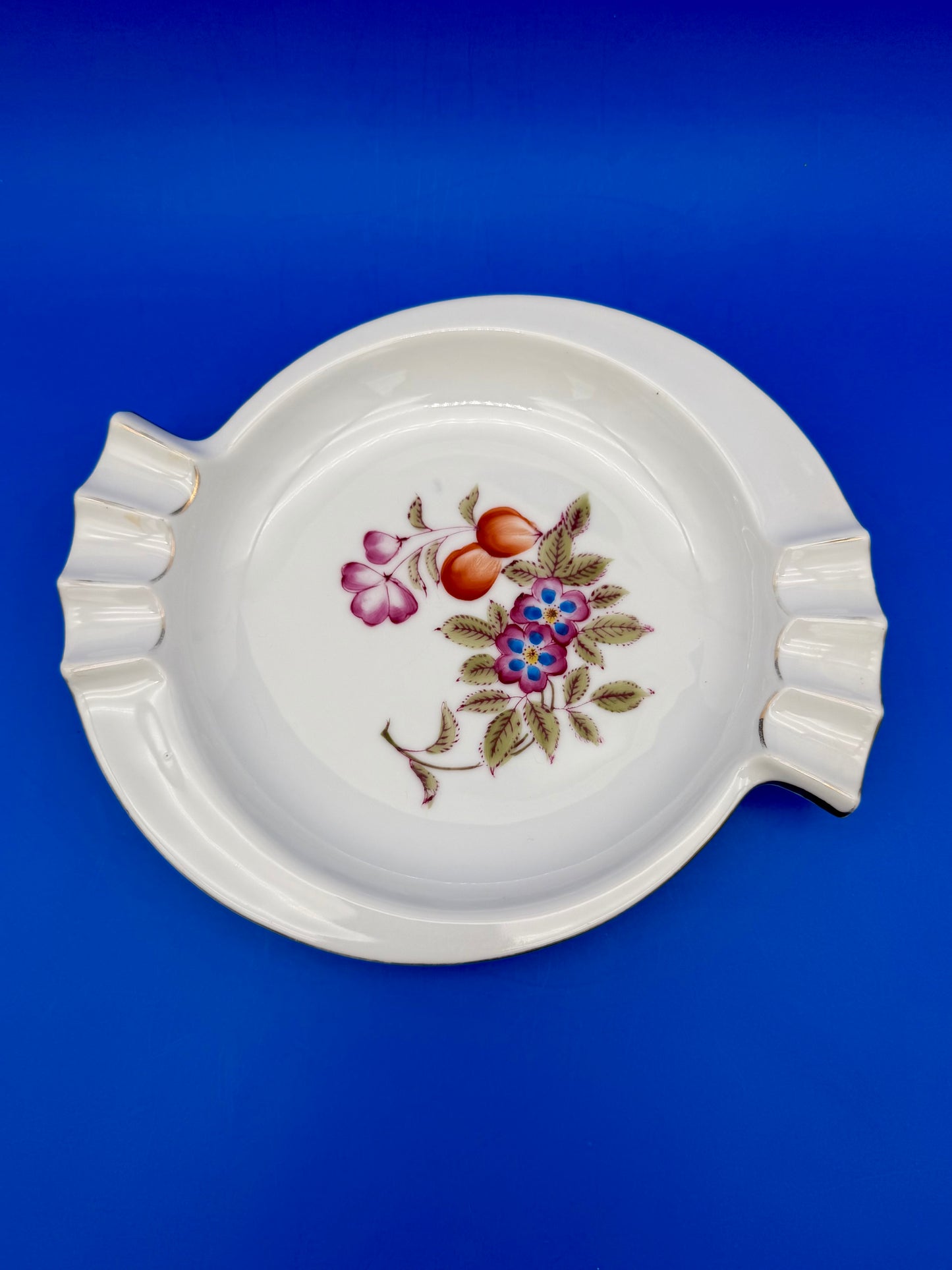 White porcelain floral ashtray viewed from above, blue background