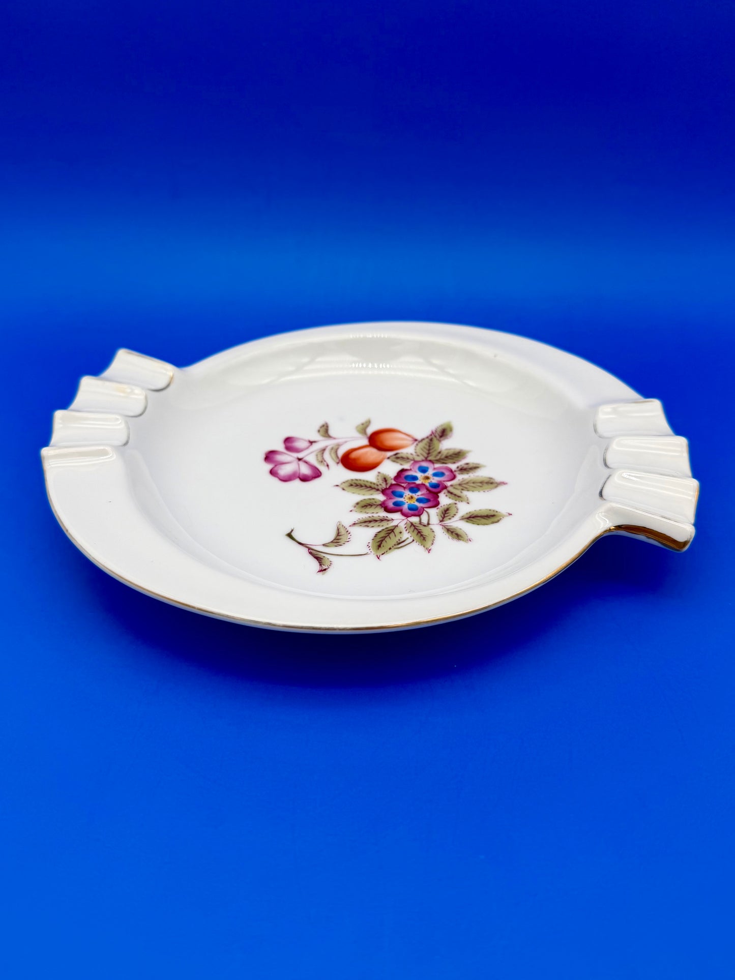 White porcelain floral ashtray shown at an angle, blue background