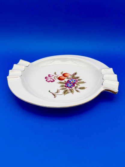 White porcelain floral ashtray shown at an angle, blue background