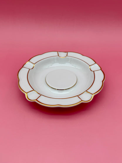 Round white ashtray with paneled scalloped border, shown at a closer angle, pink background