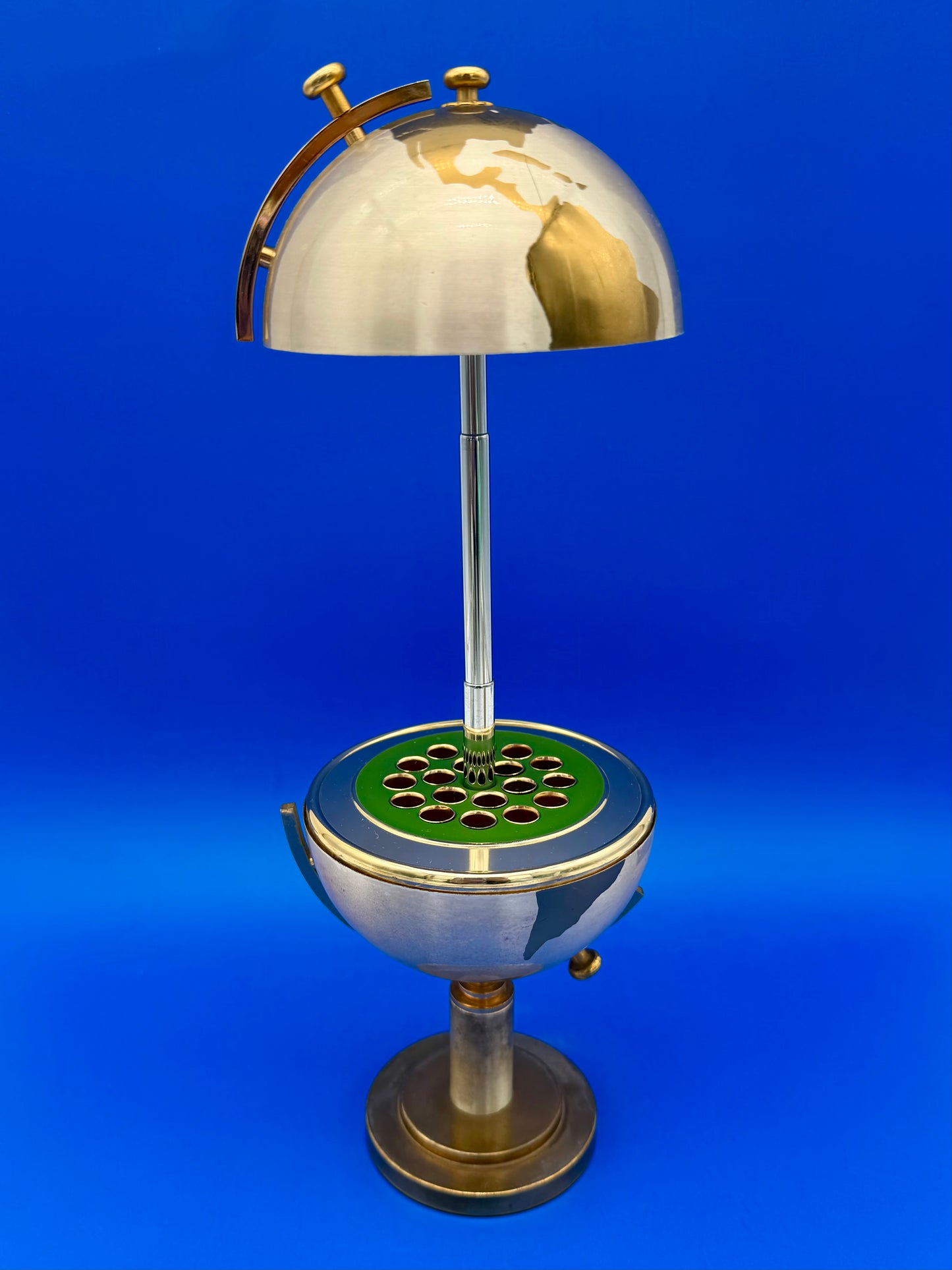 Brass globe cigarette holder open, revealing individual cigarette slots arranged around a green center