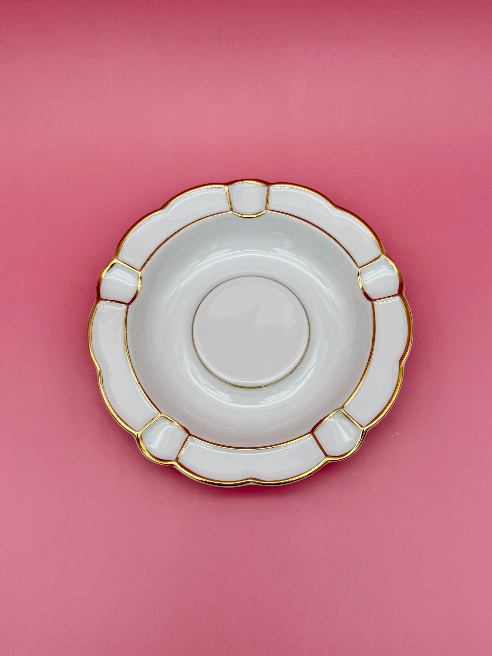 Same round white ashtray with paneled scalloped border and gold trim, shown without the cigarette pick, pink background