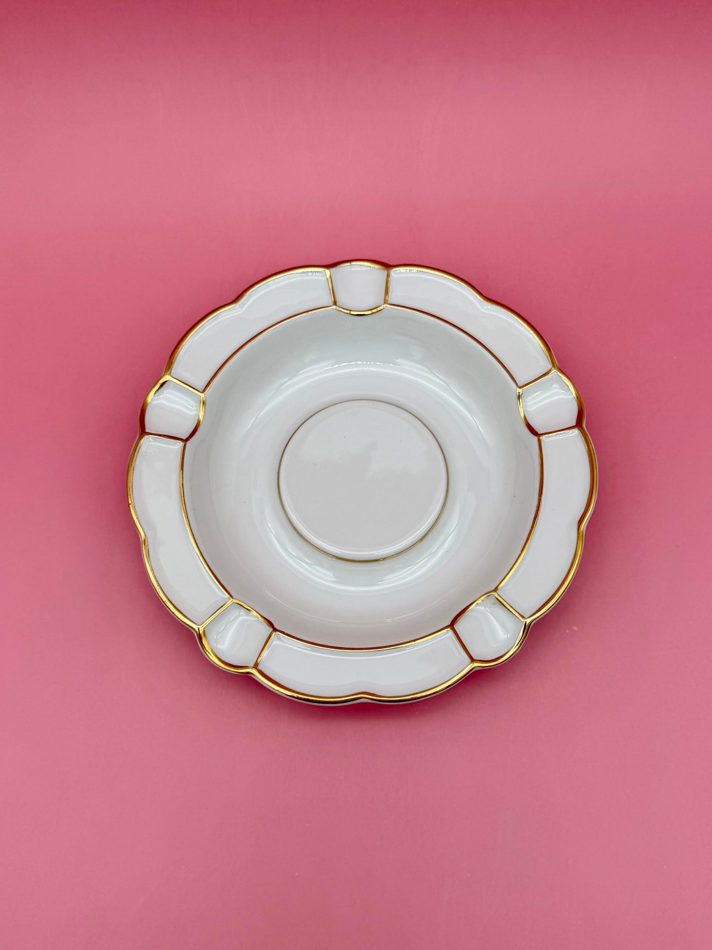 Same round white ashtray with paneled scalloped border and gold trim, shown without the cigarette pick, pink background