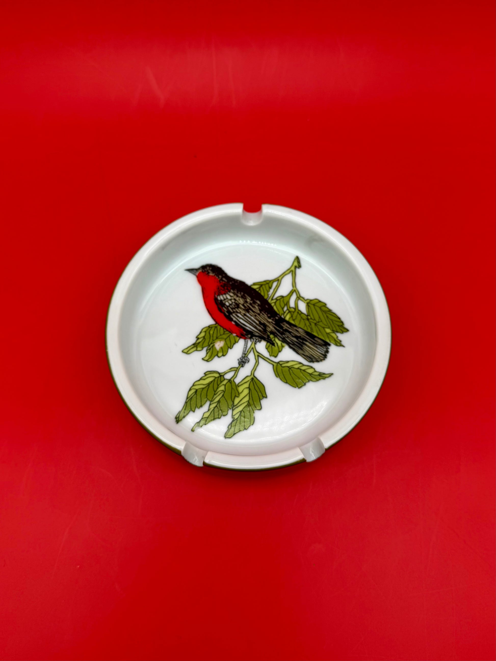 Round white ceramic ashtray hand-painted with a red robin perched on a berry branch, red background.