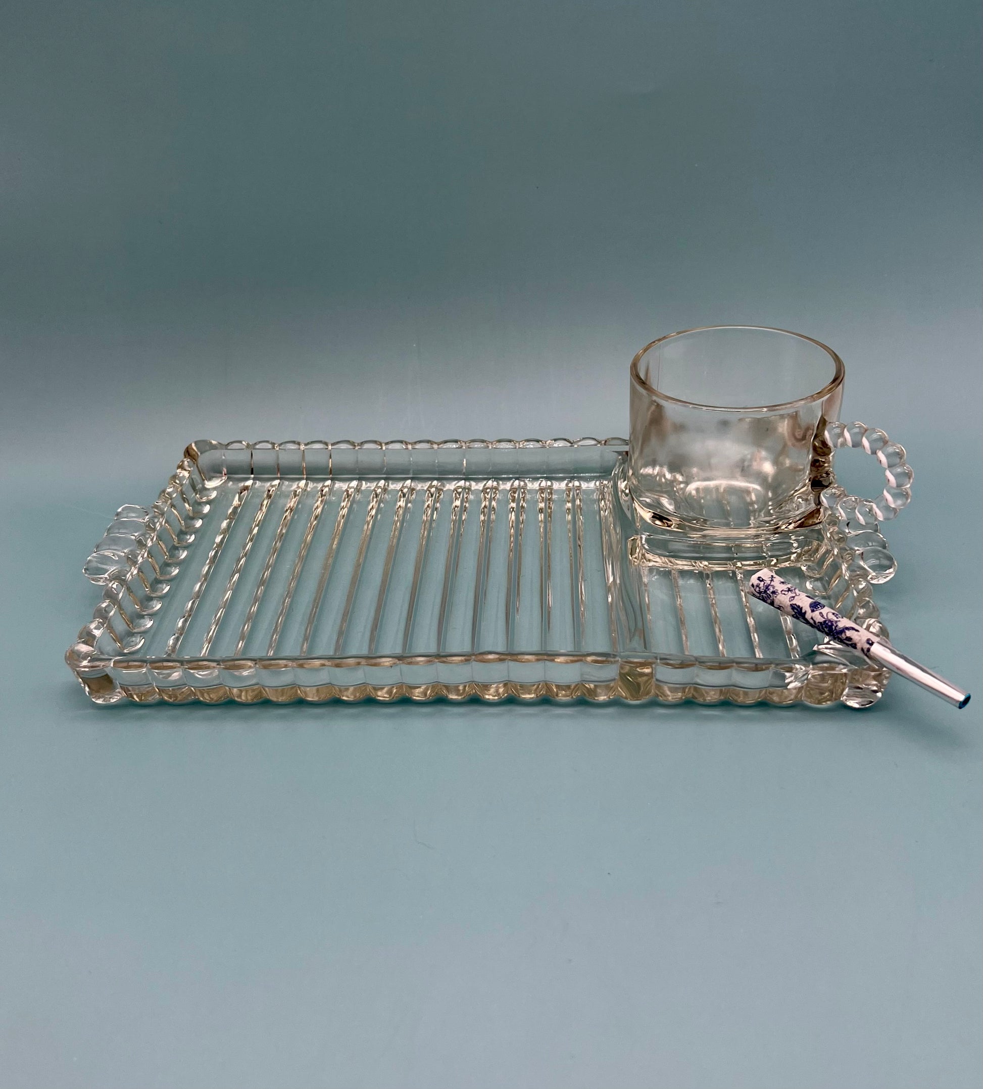 Hazel Set pressed glass snack tray with a ribbed geometric pattern, paired with a matching glass mug and glass cigarette pick, gray background.