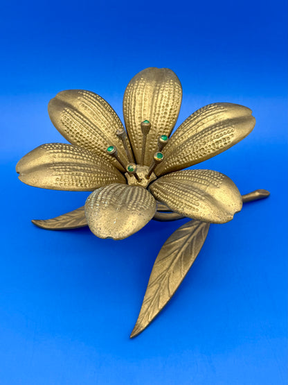Brass flower-shaped ashtray with textured petals and a leafy stem, blue background