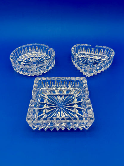Round, heart-shaped, and square faceted crystal ashtrays shown from a different angle, blue background