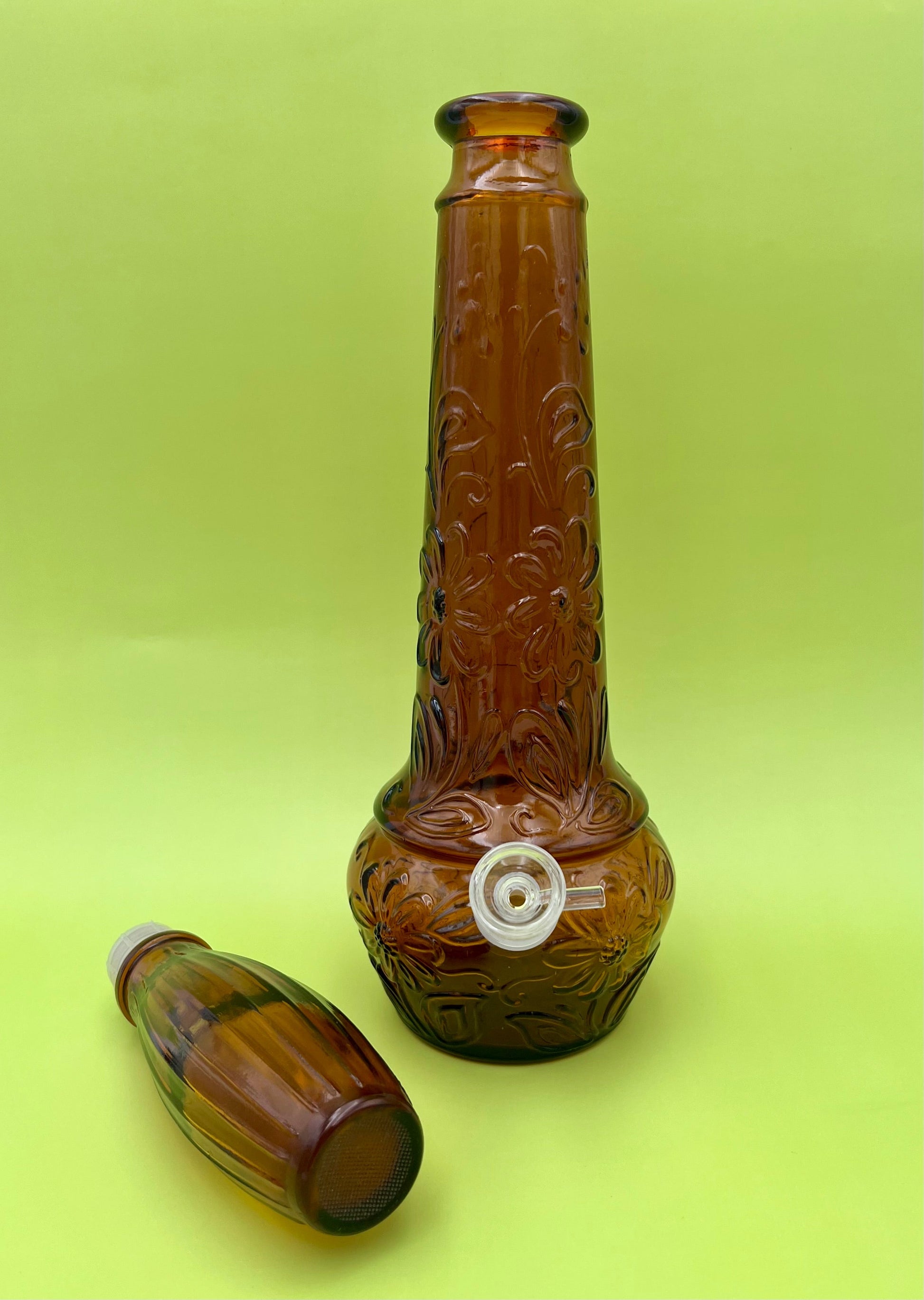 Same amber daisy-pattern genie-bottle decanter with the ribbed stopper removed and set beside the base, chartreuse background