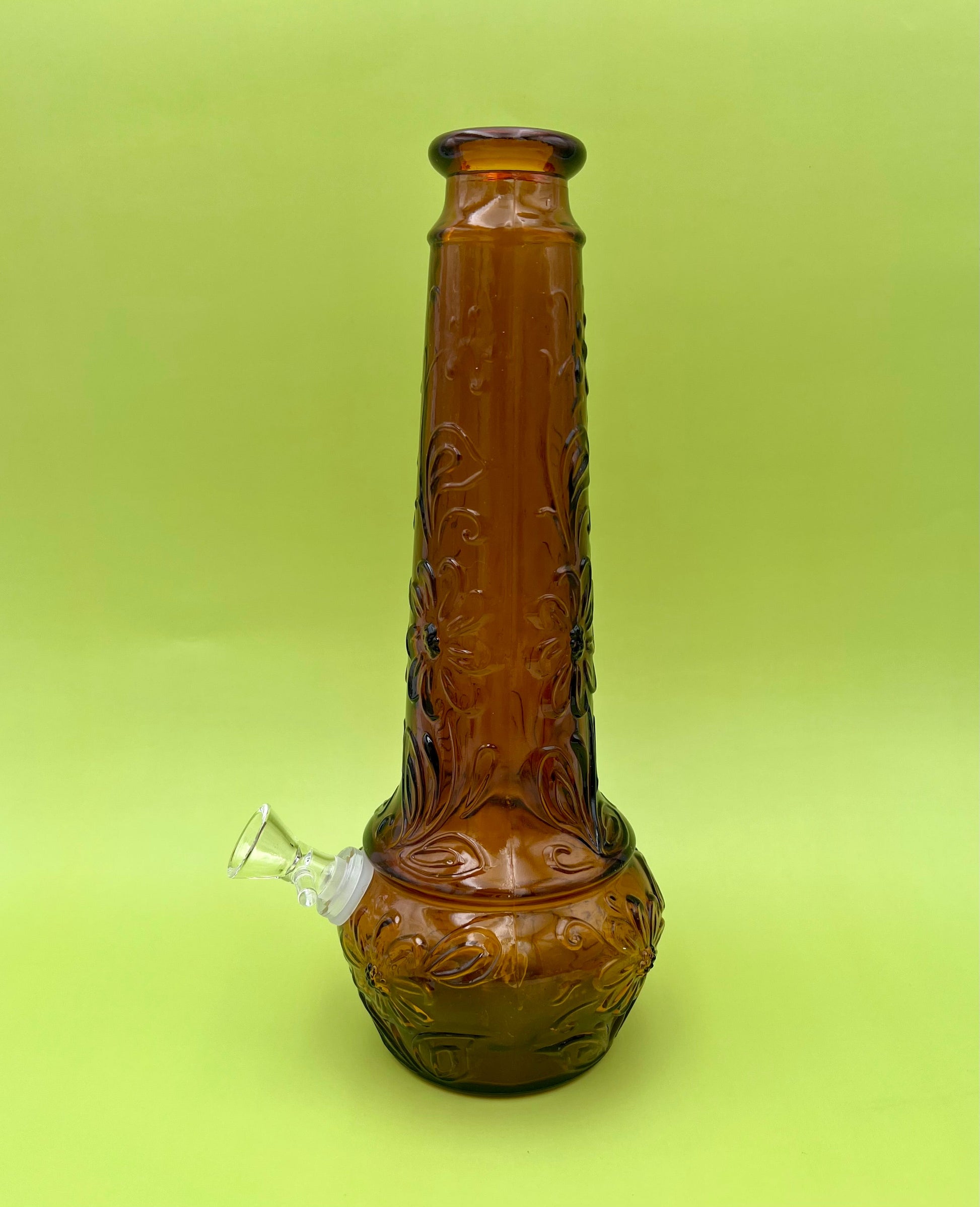 Close-up of the amber daisy-pattern decanter's base showing the embossed texture and a small paper tag, chartreuse background