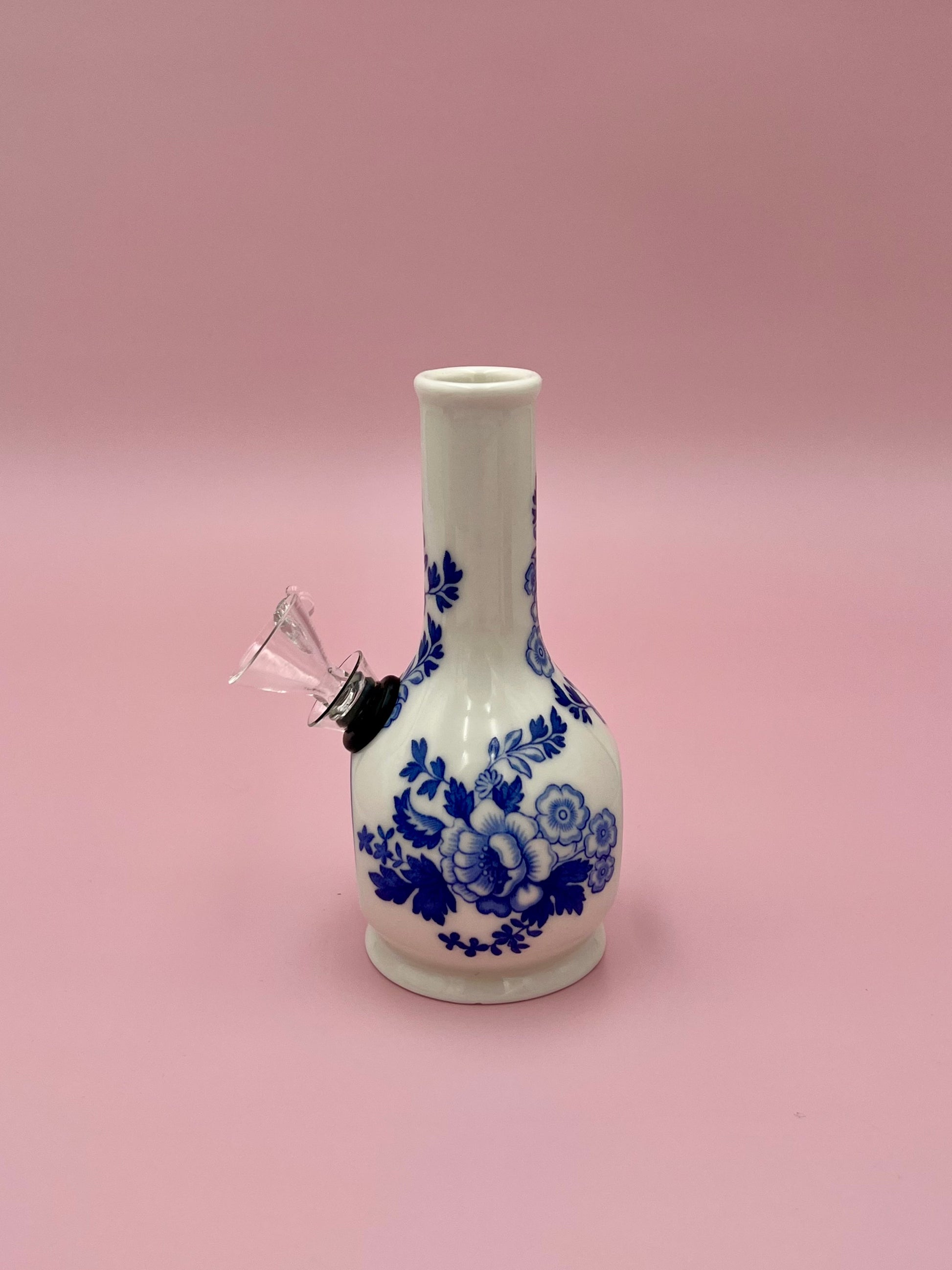 Side view of the Betty water pipe showing the glass bowl and mouthpiece fittings against the blue floral design, pink background.